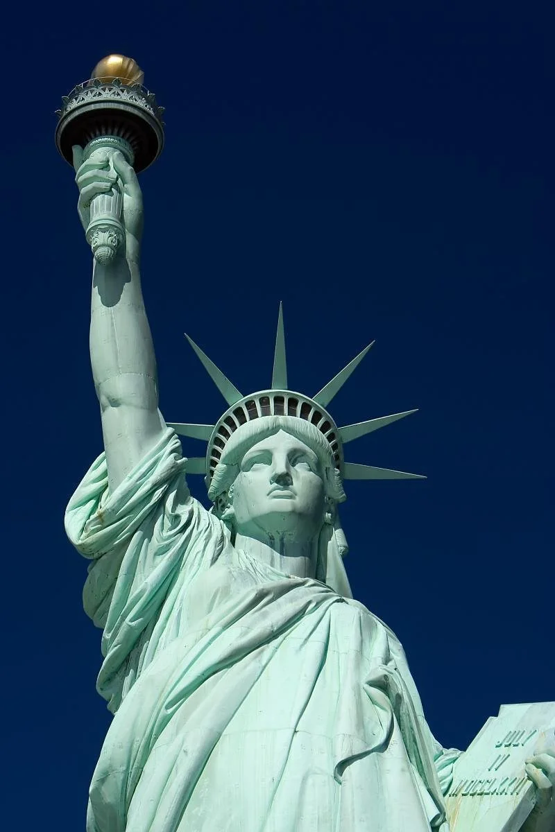 Close-up of the Statue of Liberty's head and torch against a clear dark blue sky.
