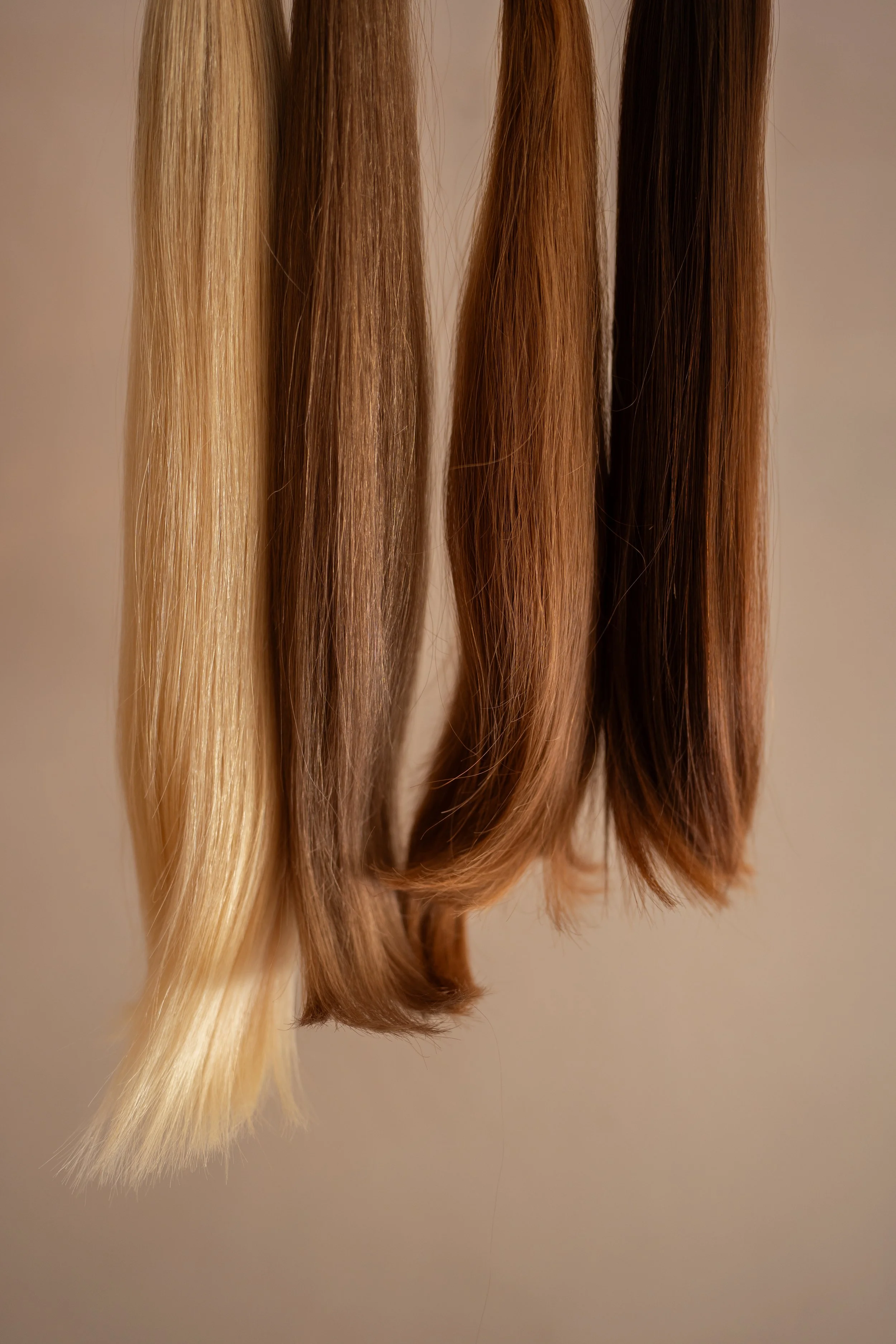 Três fios de cabelo de cores diferentes pendurados, do loiro ao castanho escuro.