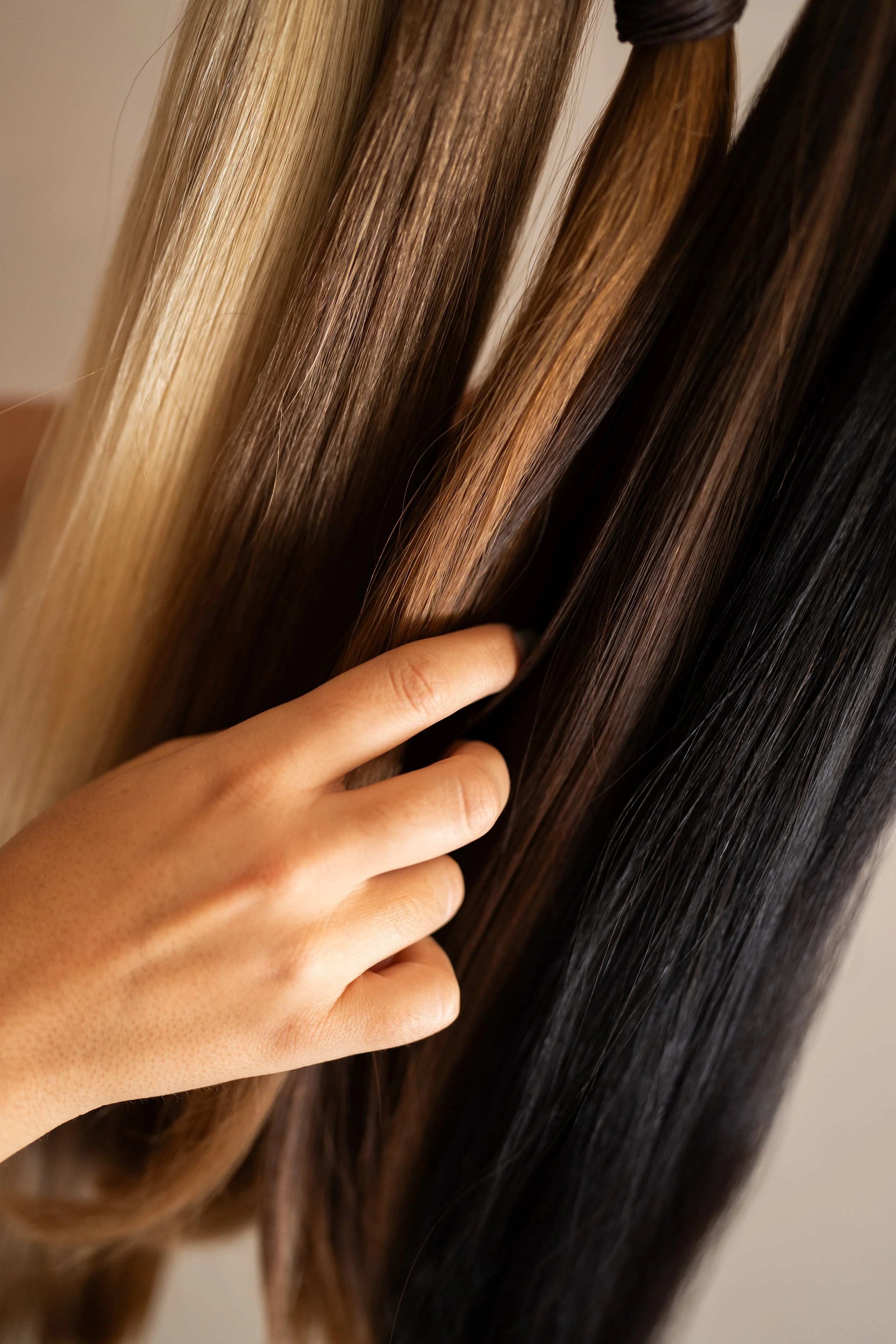 Mão tocando cabelo castanho claro, castanho escuro e preto, com cabelo liso e brilhante.