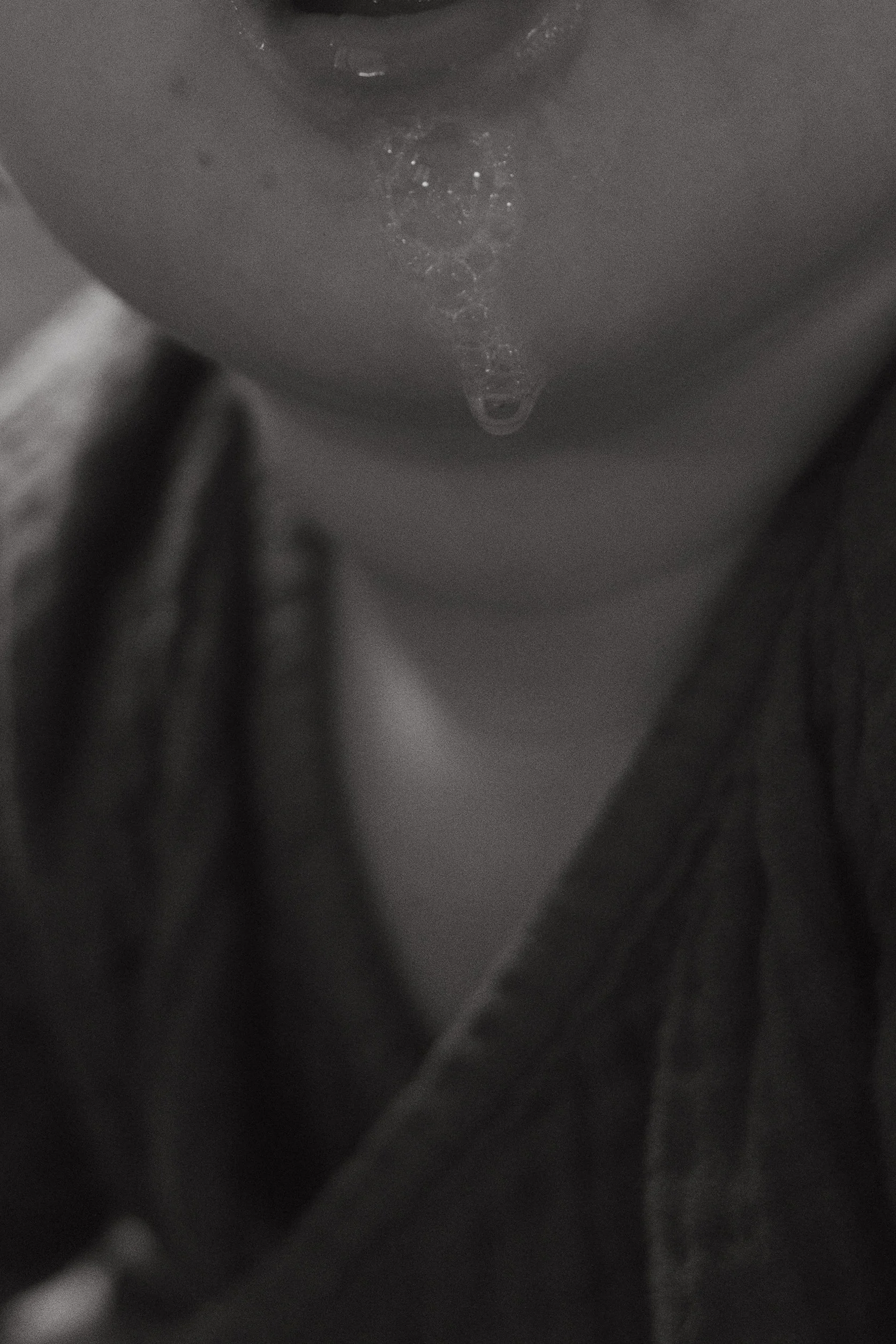 Close-up black-and-white photo of a person's face with water droplets on their chin, wearing dark clothing.
