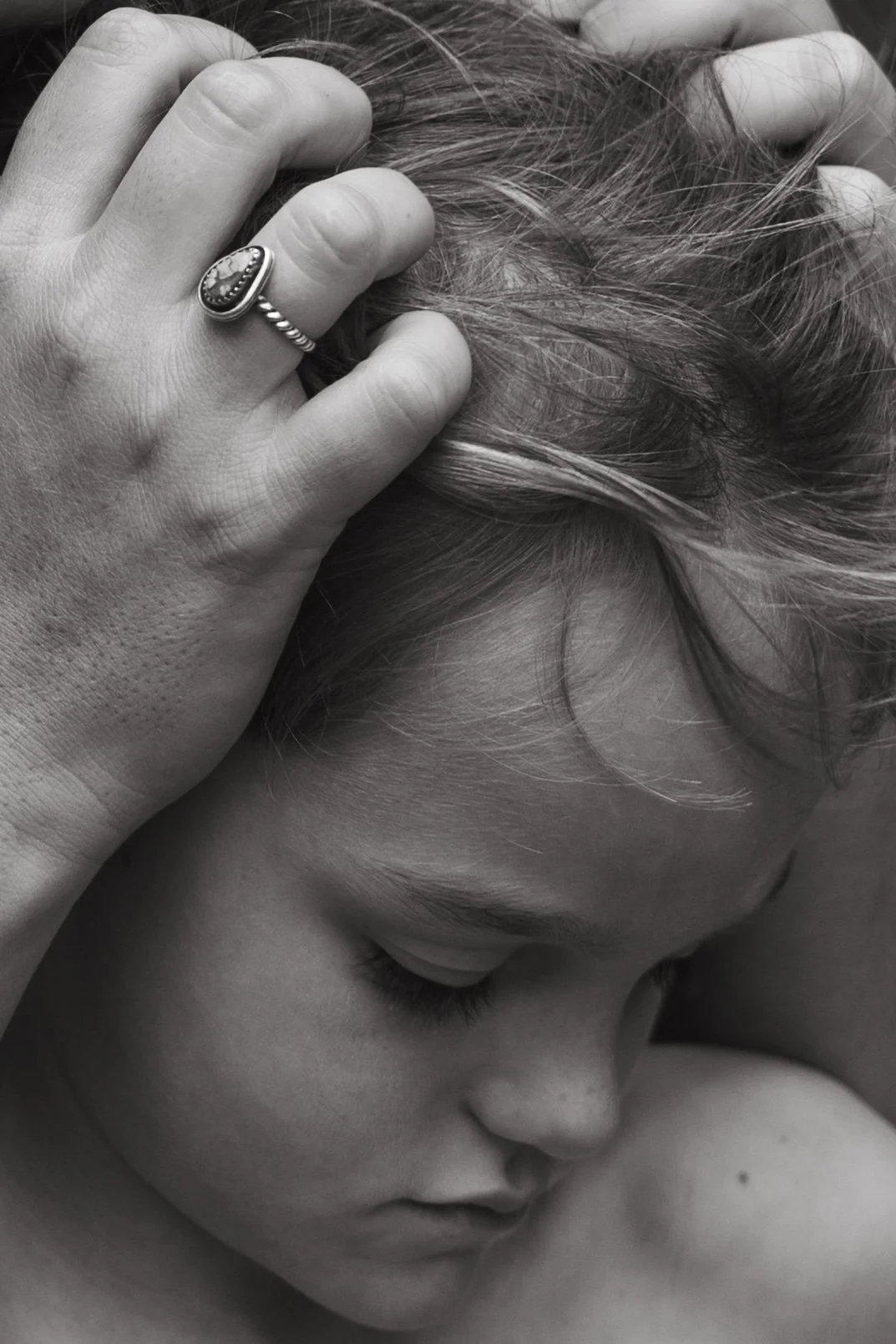Close-up of a woman with closed eyes, holding her head with one hand, wearing a ring. Black and white photograph.
