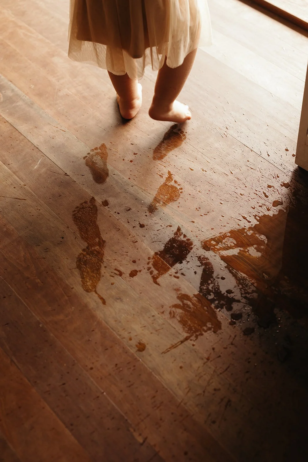 A young child with bare feet walking on a wooden floor, leaving wet footprints behind.