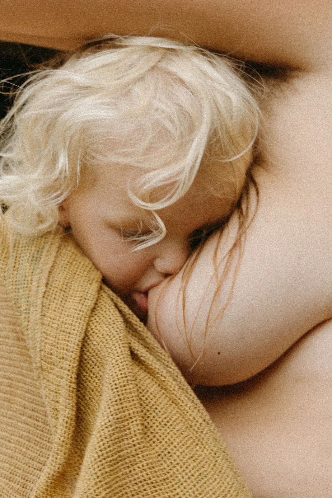 A young child with blonde curly hair peacefully sleeping with their head against an adult's chest.