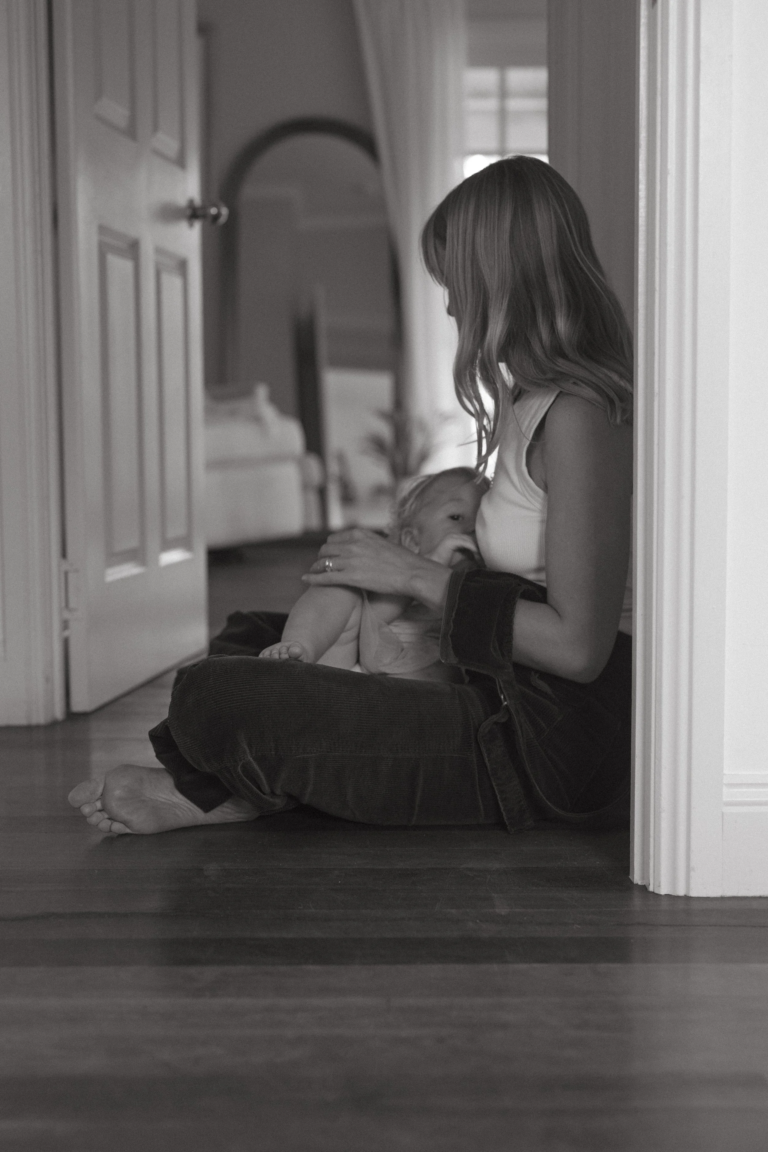 A woman sitting on the floor of a home, breastfeeding a young child in a serene, intimate moment.