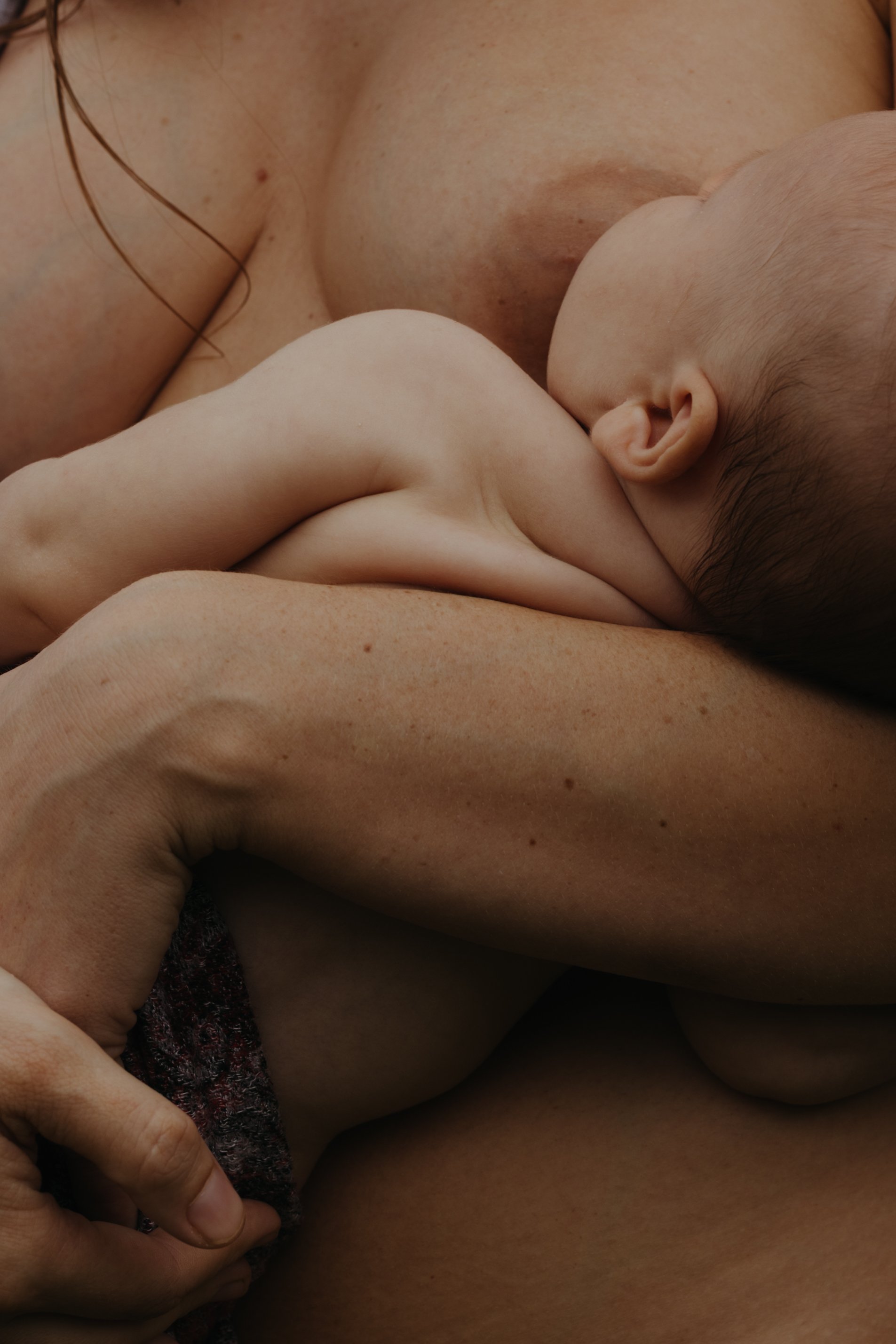 Close-up of a mother breastfeeding her baby, showing the baby nursing on her breast with her hand holding a cloth.