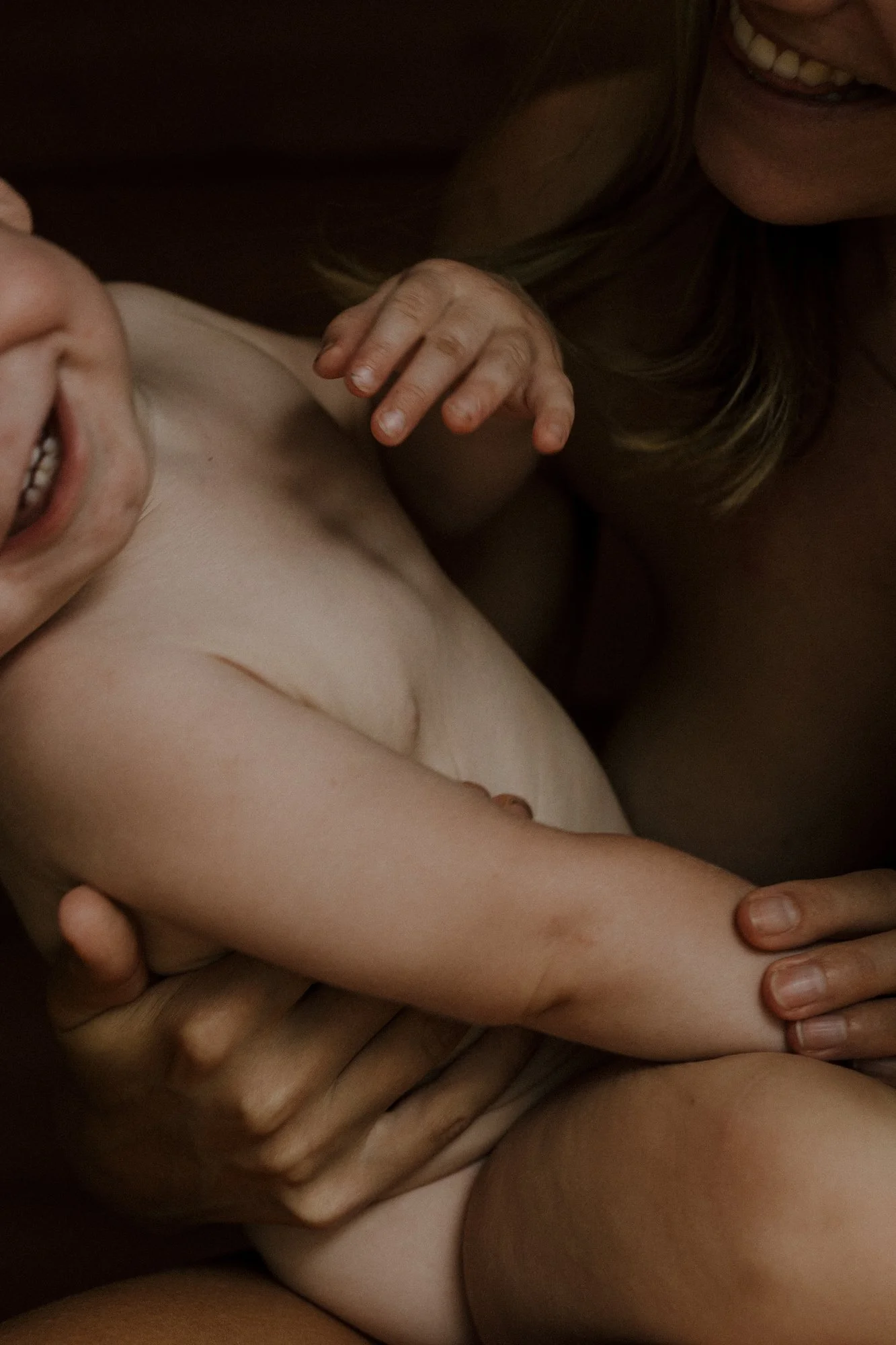 Close-up of a woman and child sharing a joyful, intimate moment, with the woman smiling and the child laughing, both partly visible and intertwined in a playful embrace.