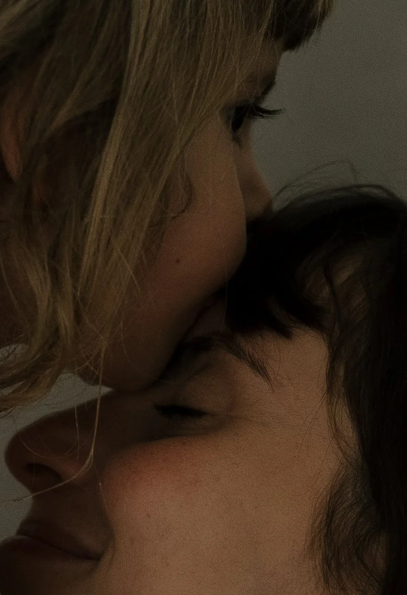 Close-up of two people sharing an intimate kiss, with only their faces and closed eyes visible, in a dimly lit setting.