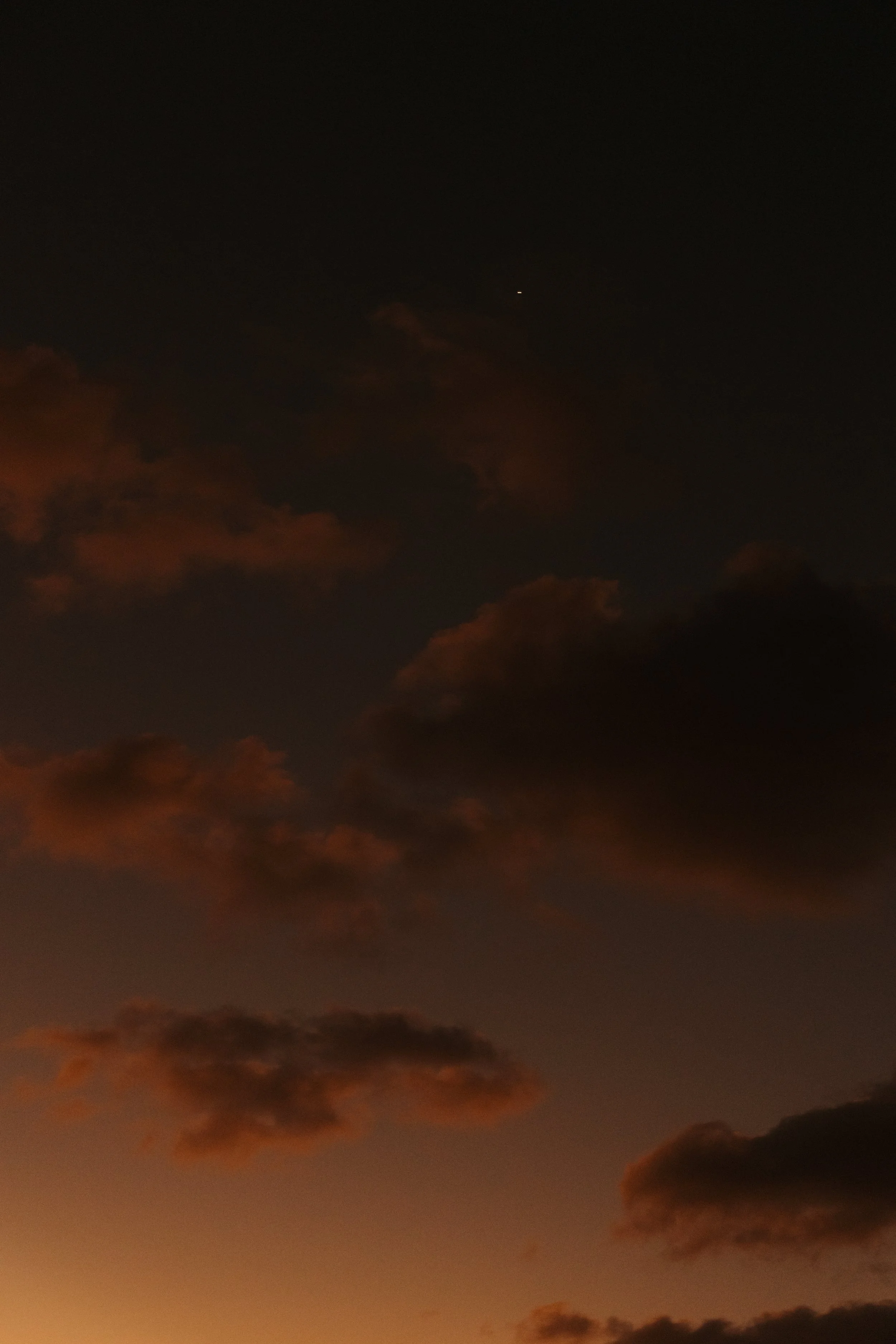 Dark sky with orange and pink clouds at sunset or dusk.
