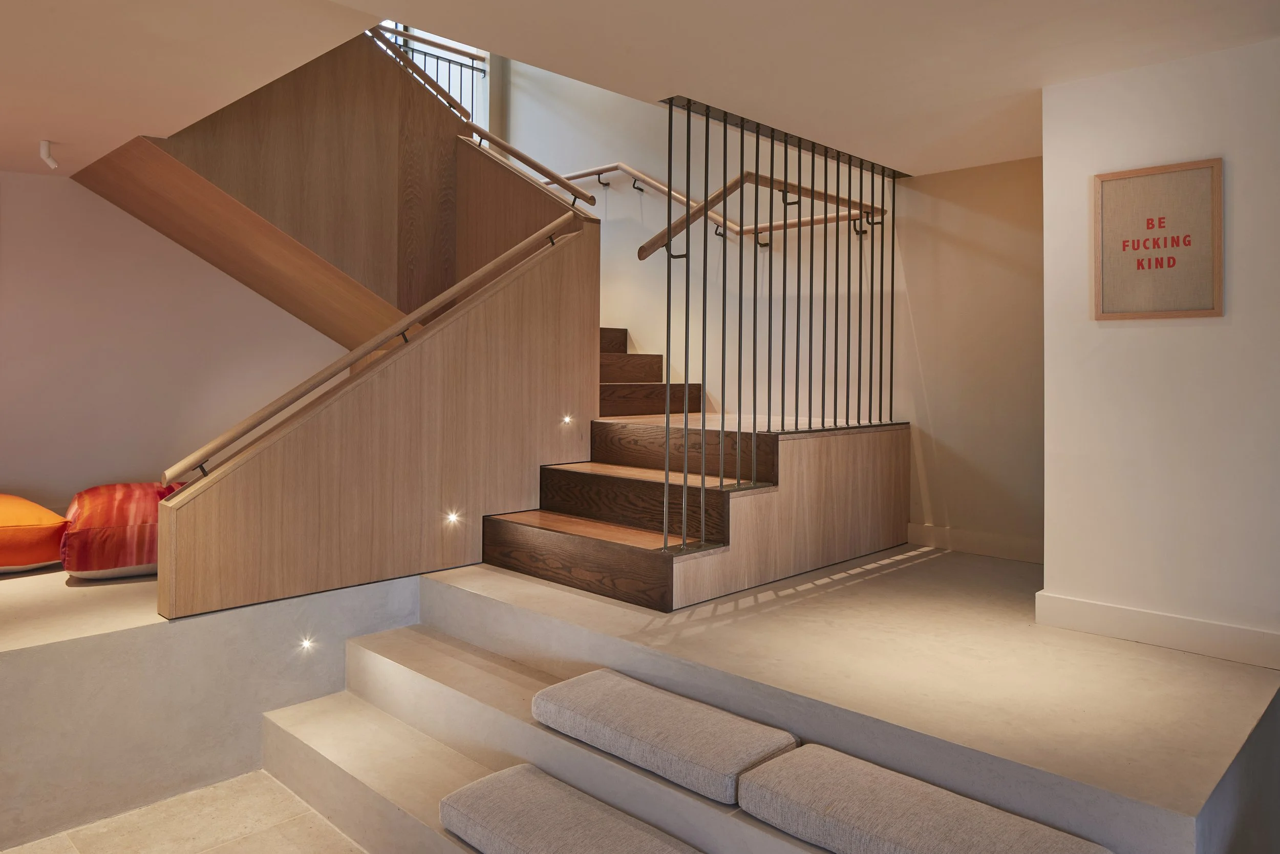 Orme Ltd — Interior view of a modern staircase with wooden steps, black metal railing, and wooden paneling, accented with small built-in lights.