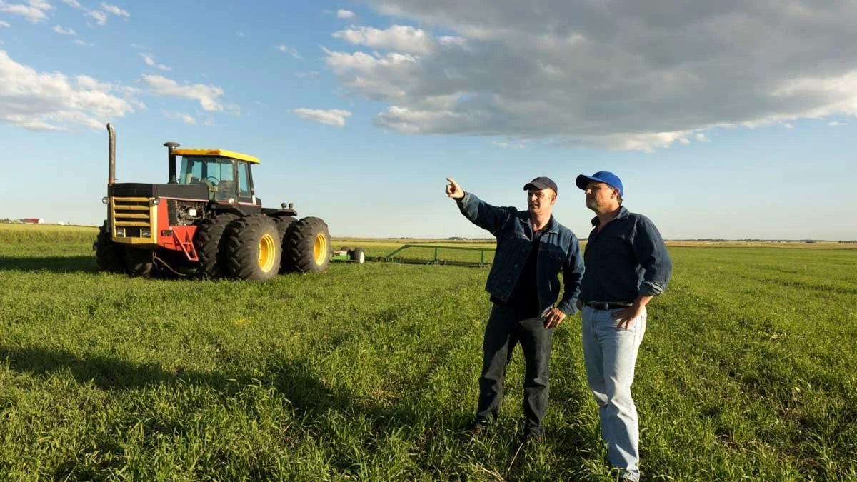 Two farmers talking in a green paddock beside a large tractor