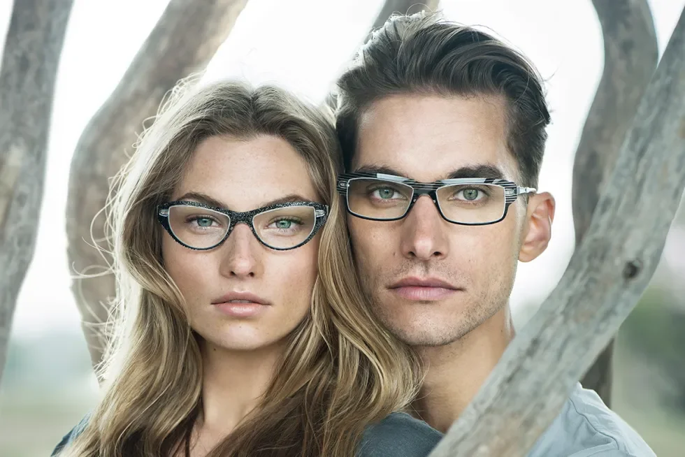 A young man and woman wearing glasses standing outdoors near tree branches