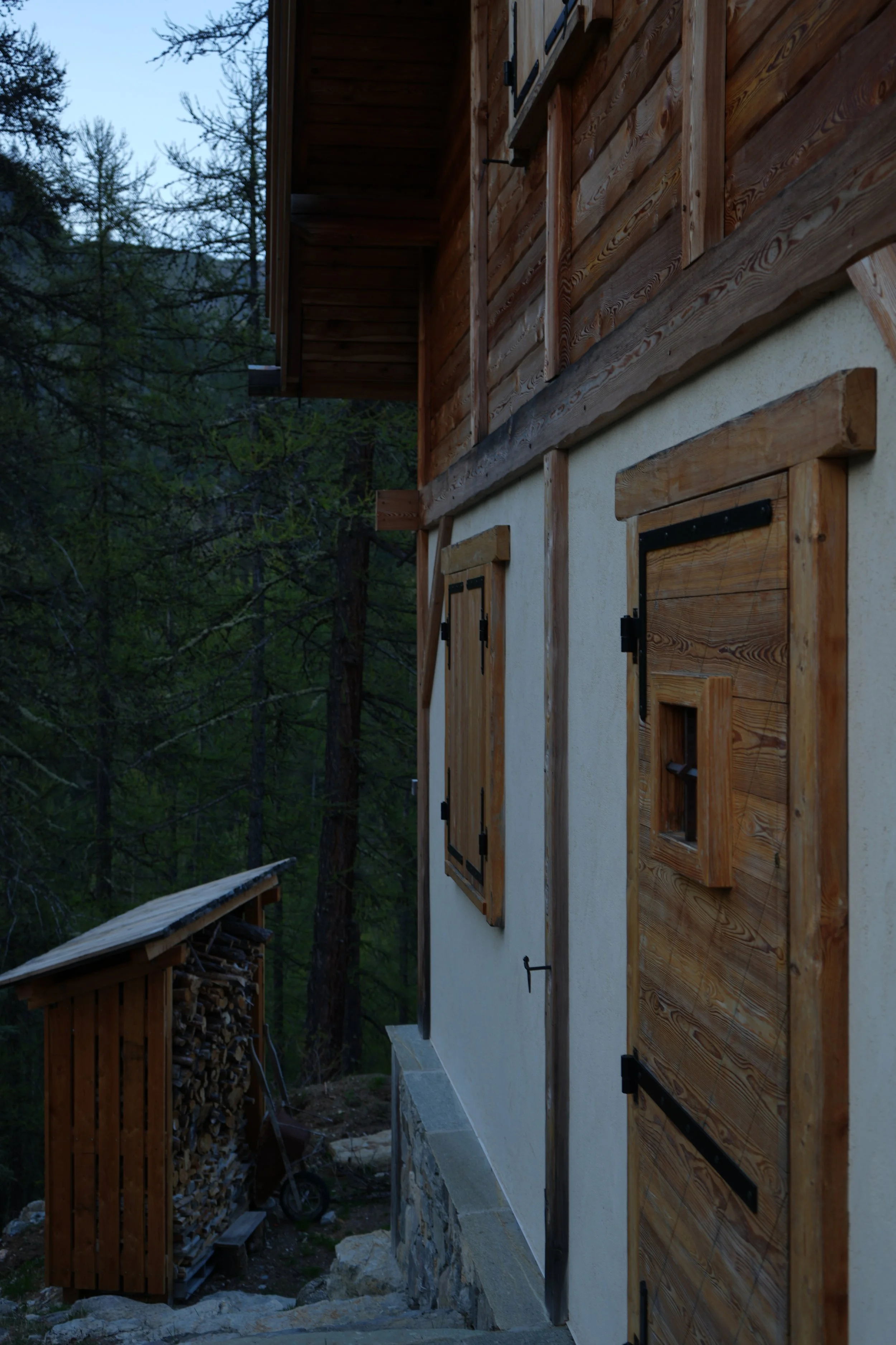 Façade d'une maison en bois avec volets en bois, entourée d'arbres dans un environnement naturel.