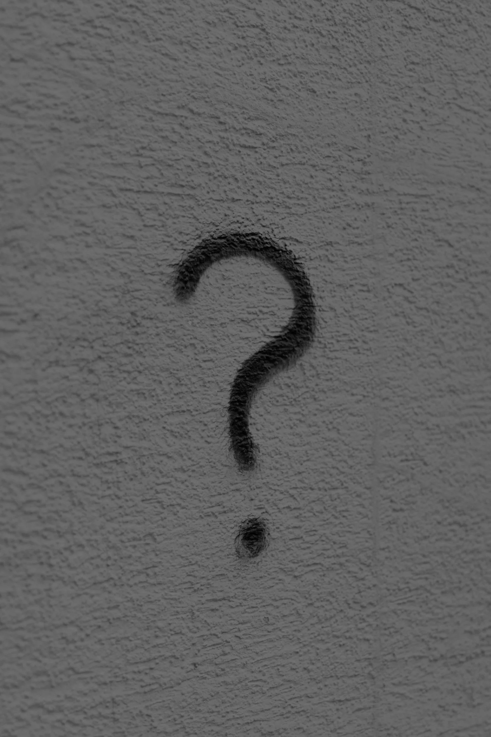 Black question mark spray-painted on a textured wall.