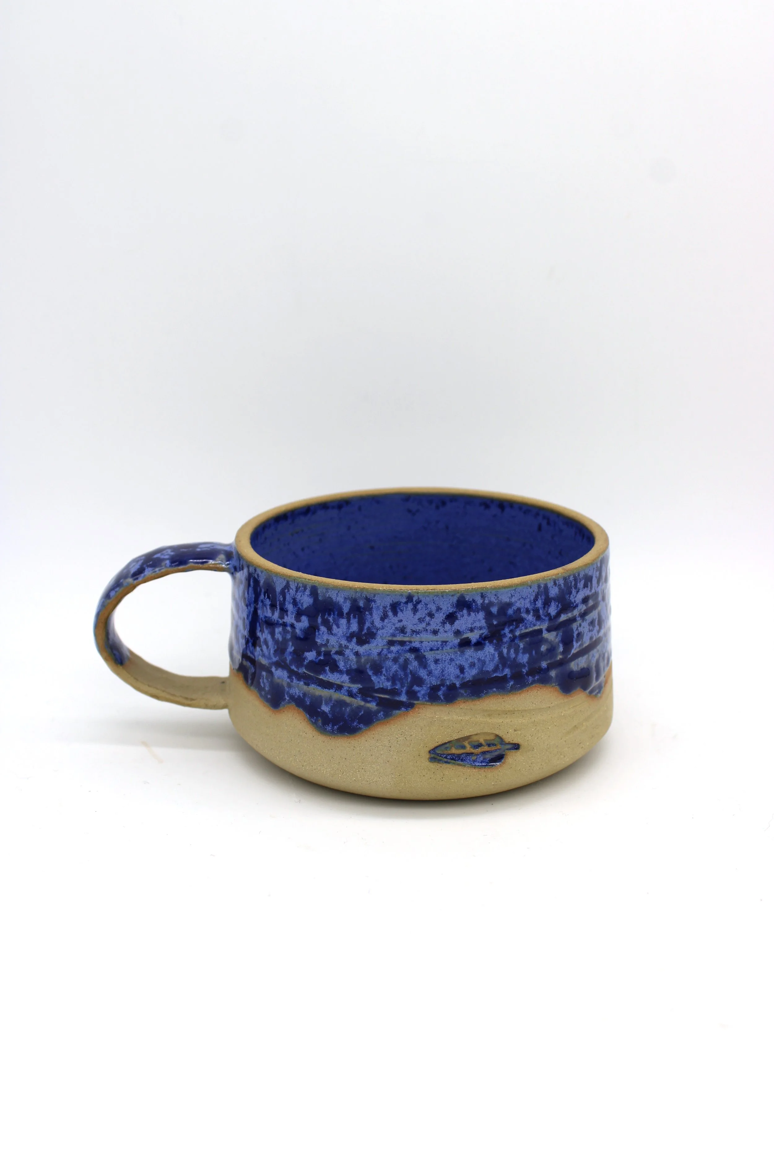 Ceramic mug with a beige base and black speckles, decorated with blue glaze that drips from the rim.