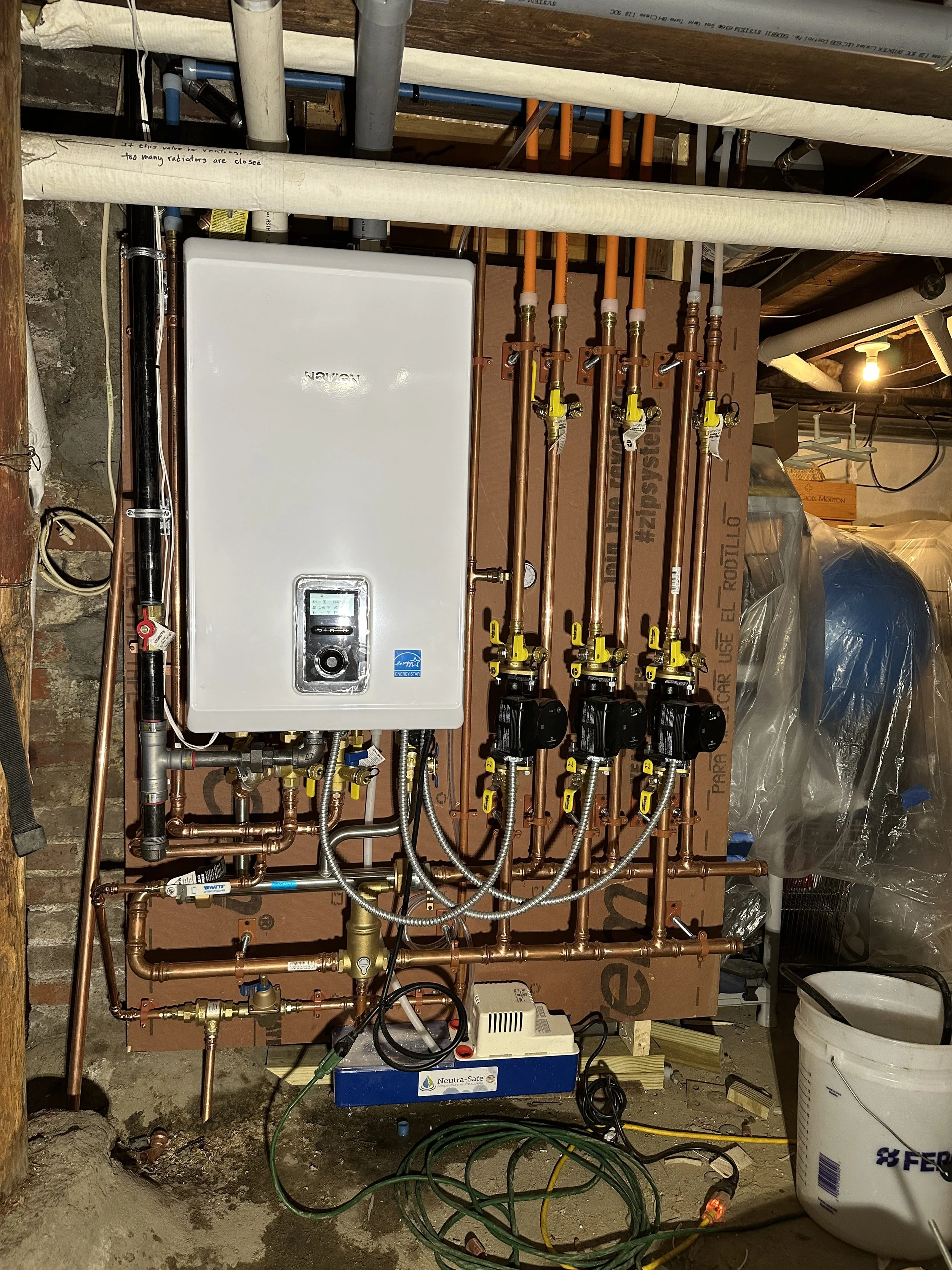 A plumbing installation showing a white boiler, copper pipes, and valves in a basement setting.