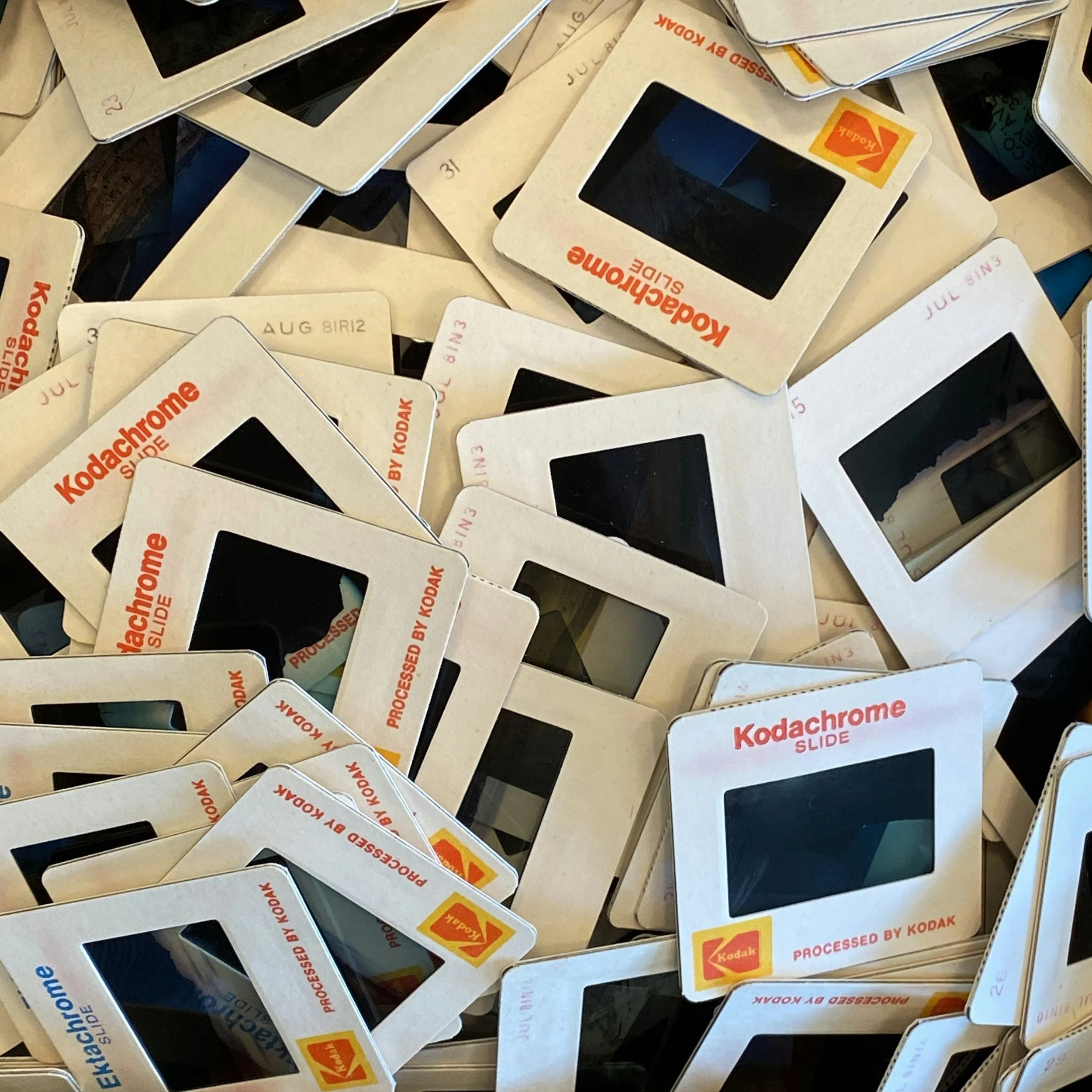 A pile of vintage Kodak Kodachrome SLIDE mounts with color logos and black slides, arranged randomly.