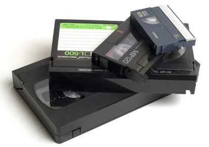 Stack of VHS tapes and a VHS player on a white surface