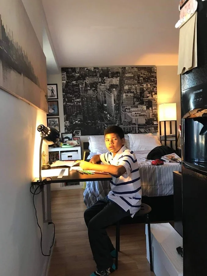 Child working at a desk in his bedroom with artwork on the wall, showing creativity, focus, and self-expression through learning.