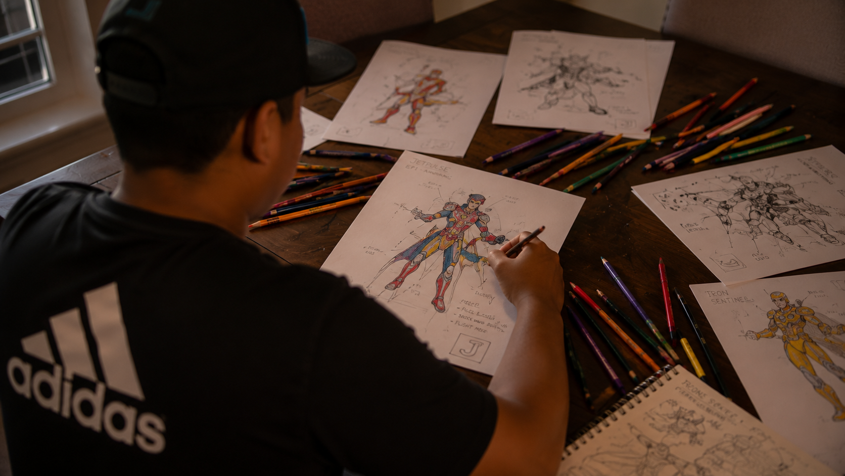 Child creating superhero character sketches at a wooden table surrounded by comic drawings, colored pencils, worksheets, and storytelling pages inside the Jetpulse creative studio.