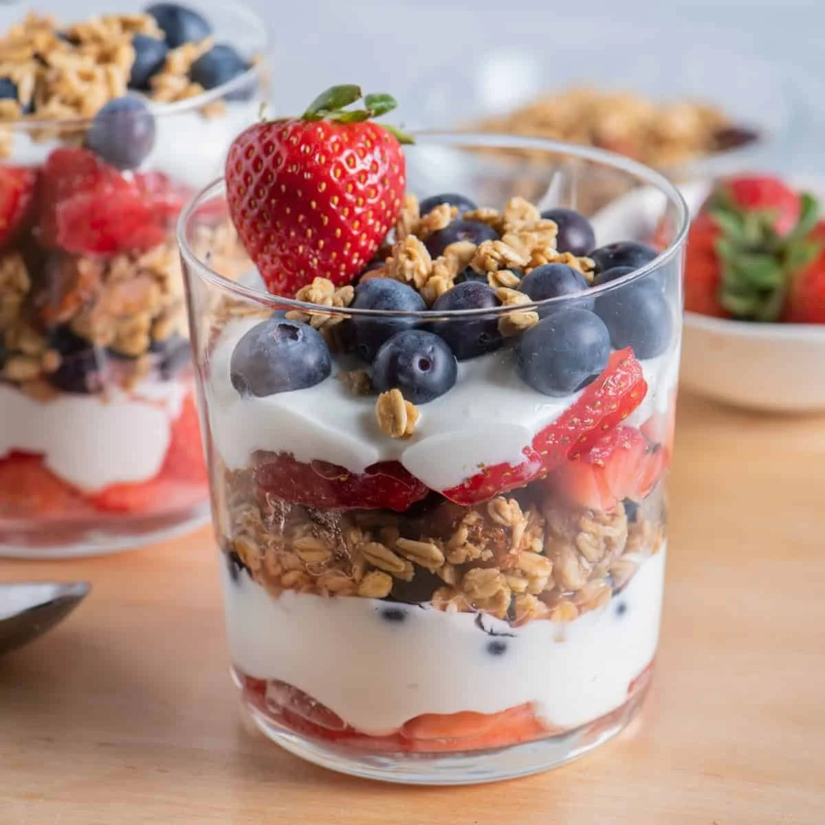 A layered yogurt parfait with strawberries, blueberries, granola, and whipped cream in a clear glass