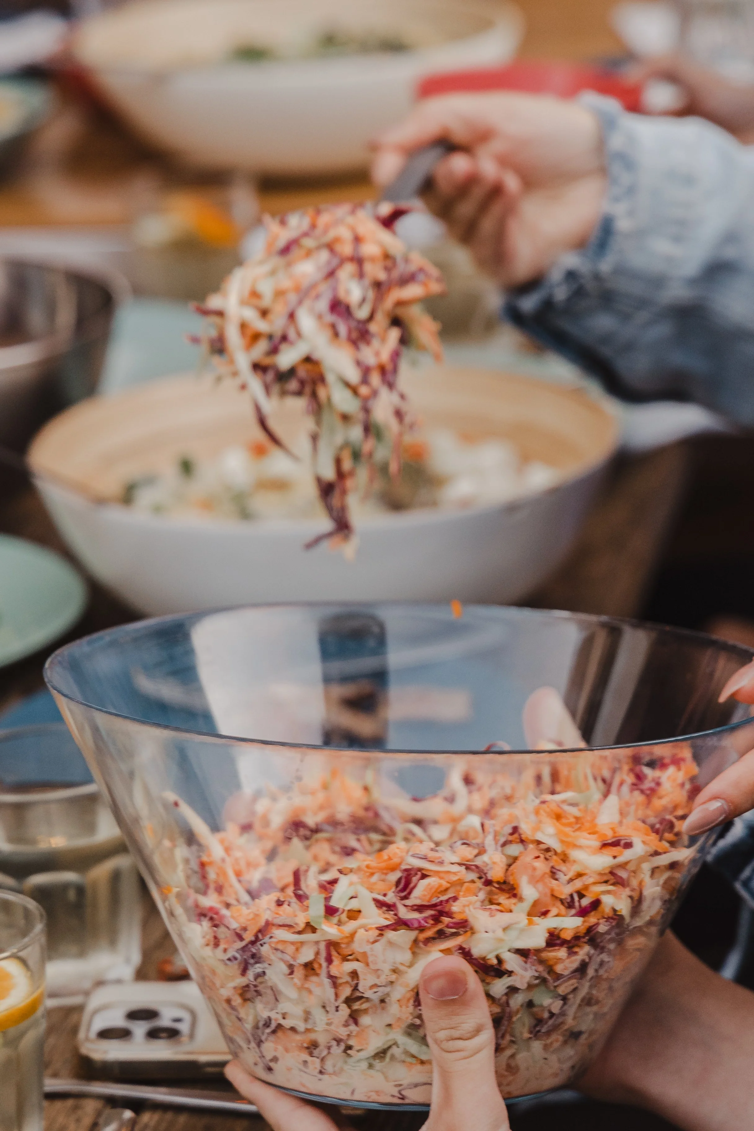 Person holding a large glass bowl of shredded vegetable salad, with another salad bowl in the background.