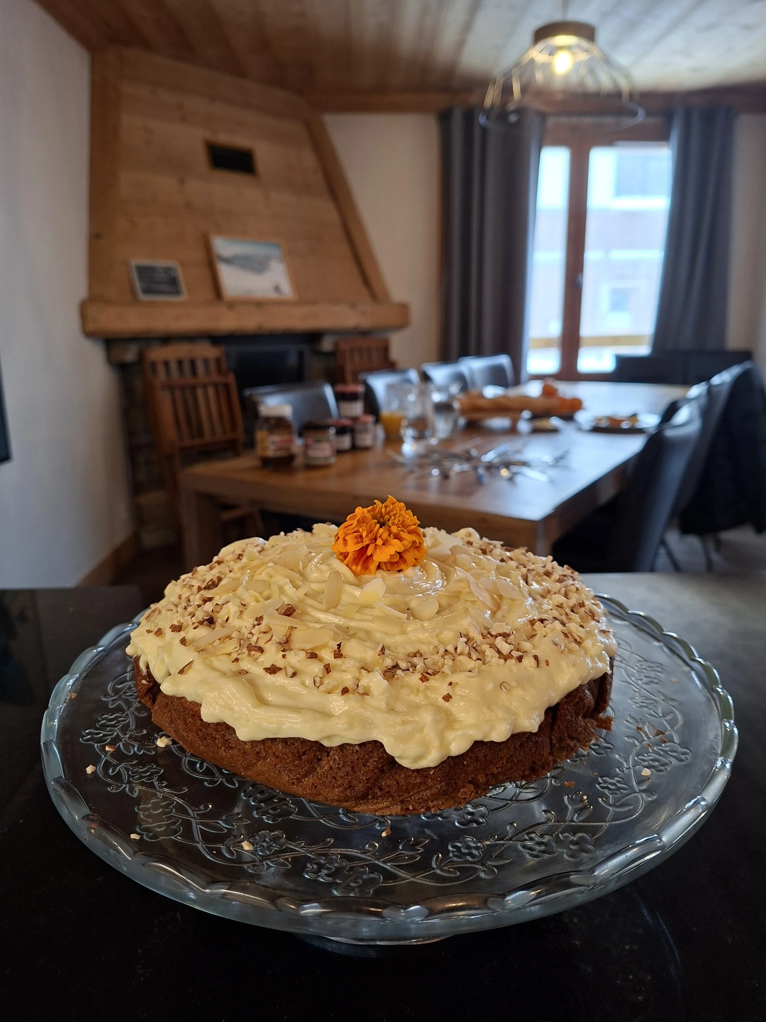 A decorated cake topped with shredded white cheese and an orange flower, sitting on a glass plate.