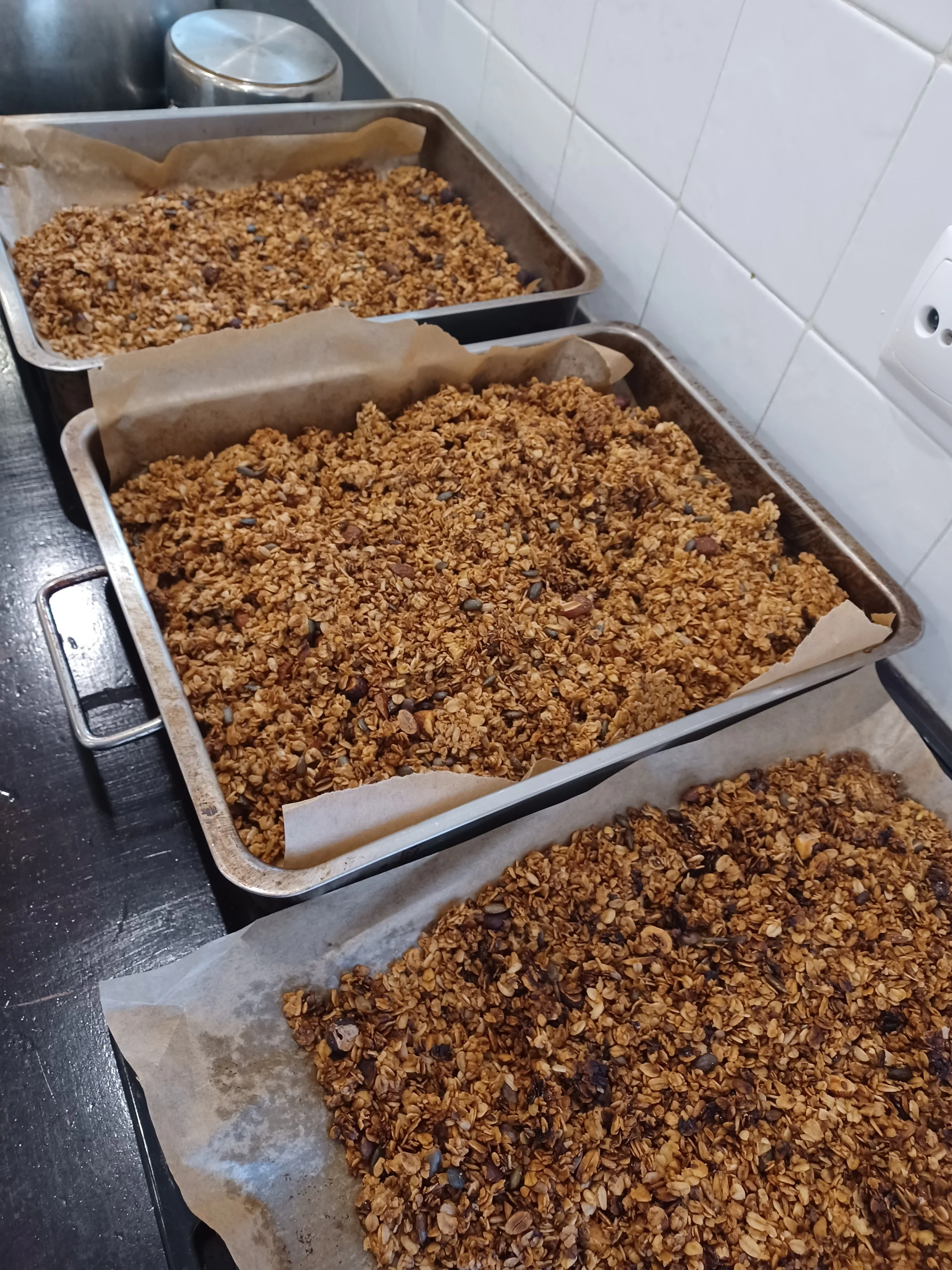 Baking trays with granola and chocolate chips on parchment paper, ready to be baked.