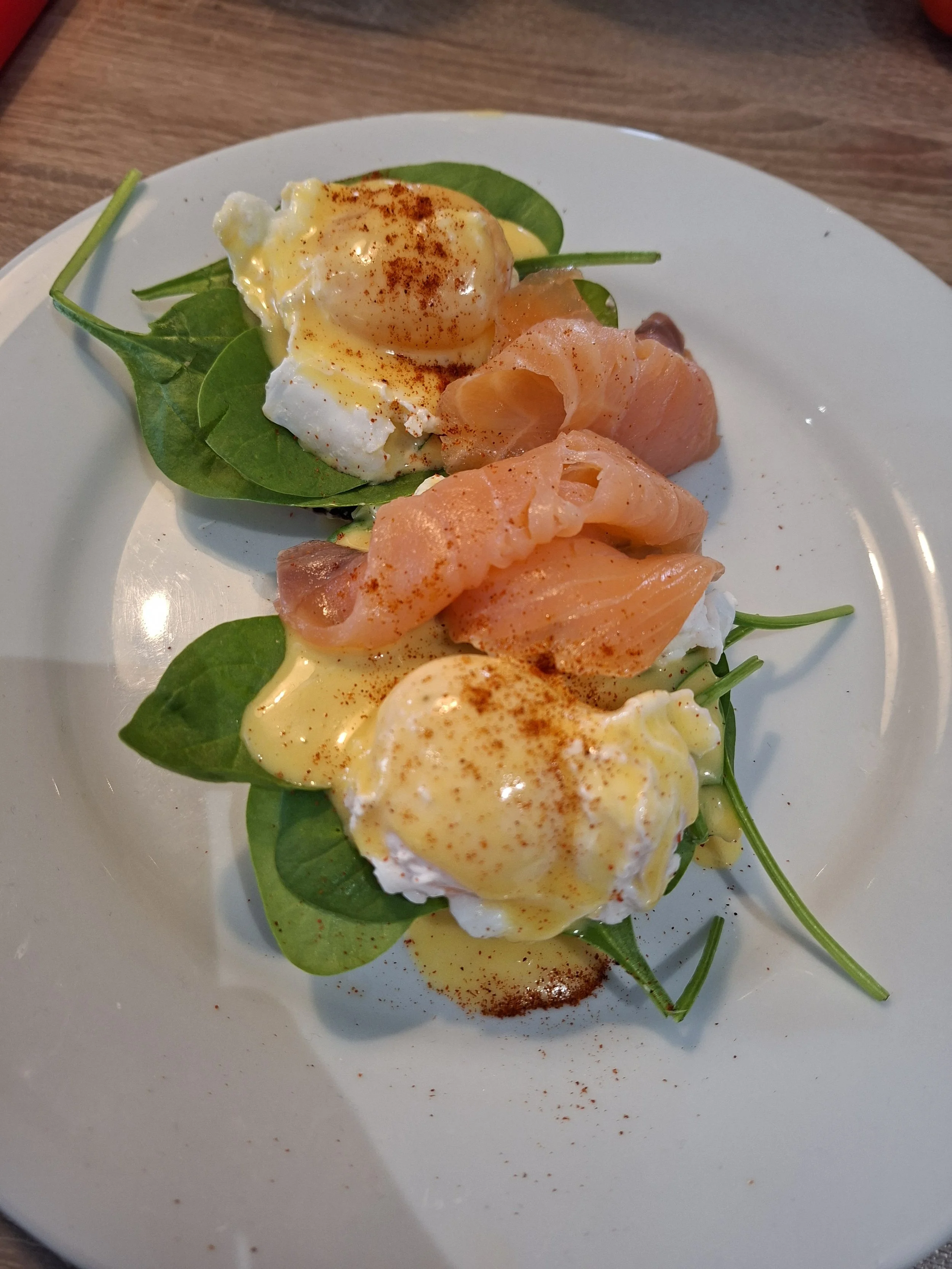 Poached eggs topped with paprika, served on a bed of spinach leaves with smoked salmon on the side, on a white plate.