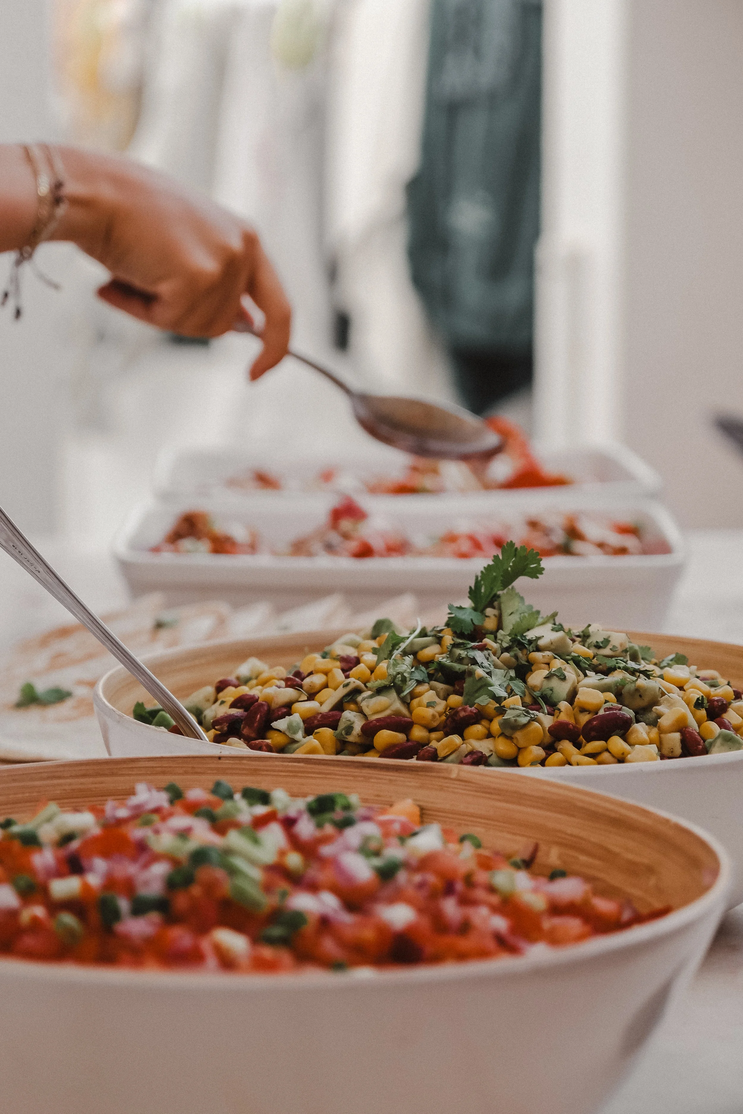 Close-up of bowls of colorful salads on a table, with a person serving food in the background.