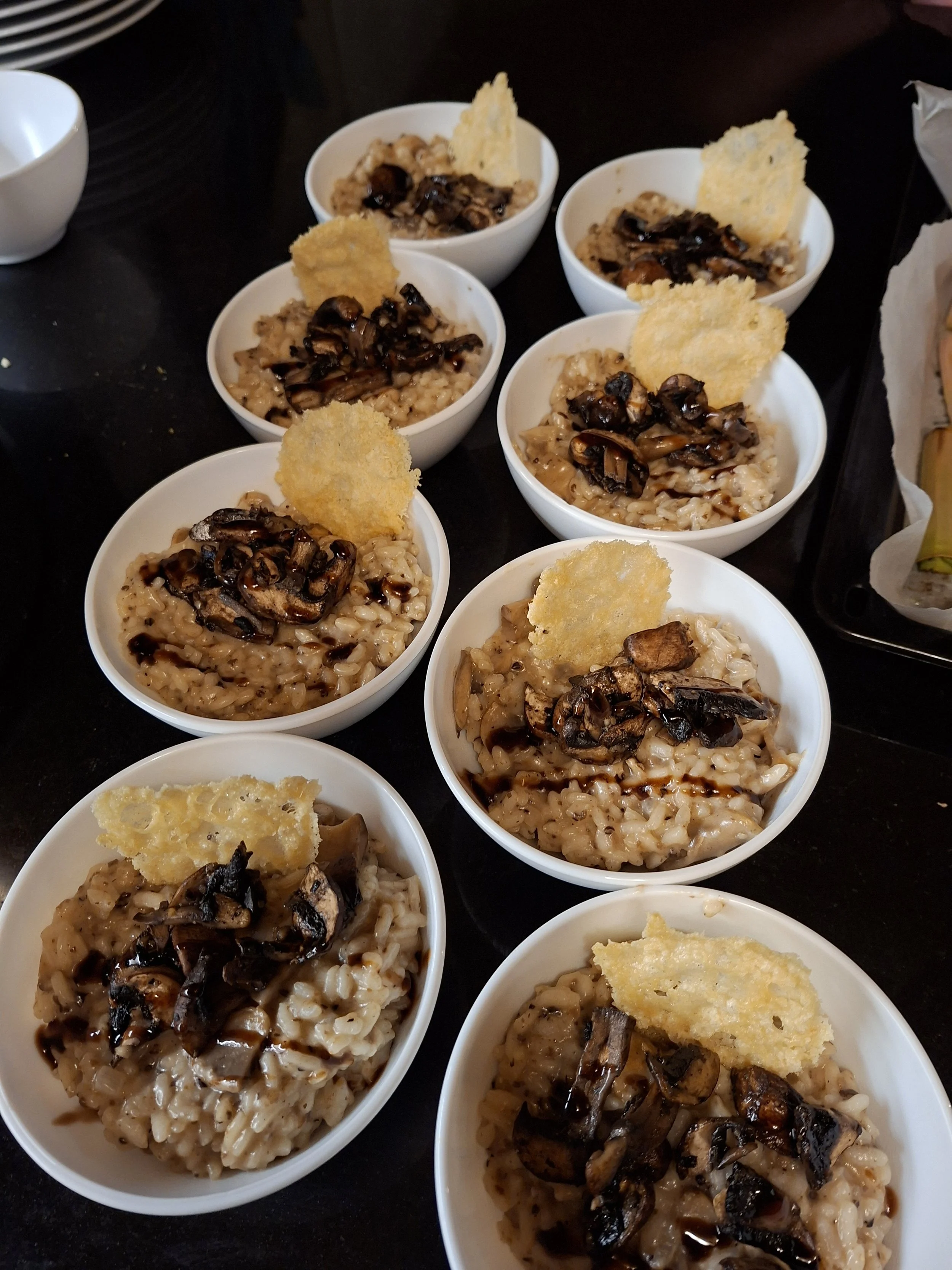 Multiple small white bowls filled with mushroom risotto topped with sautéed mushrooms and a crispy cheese chip.