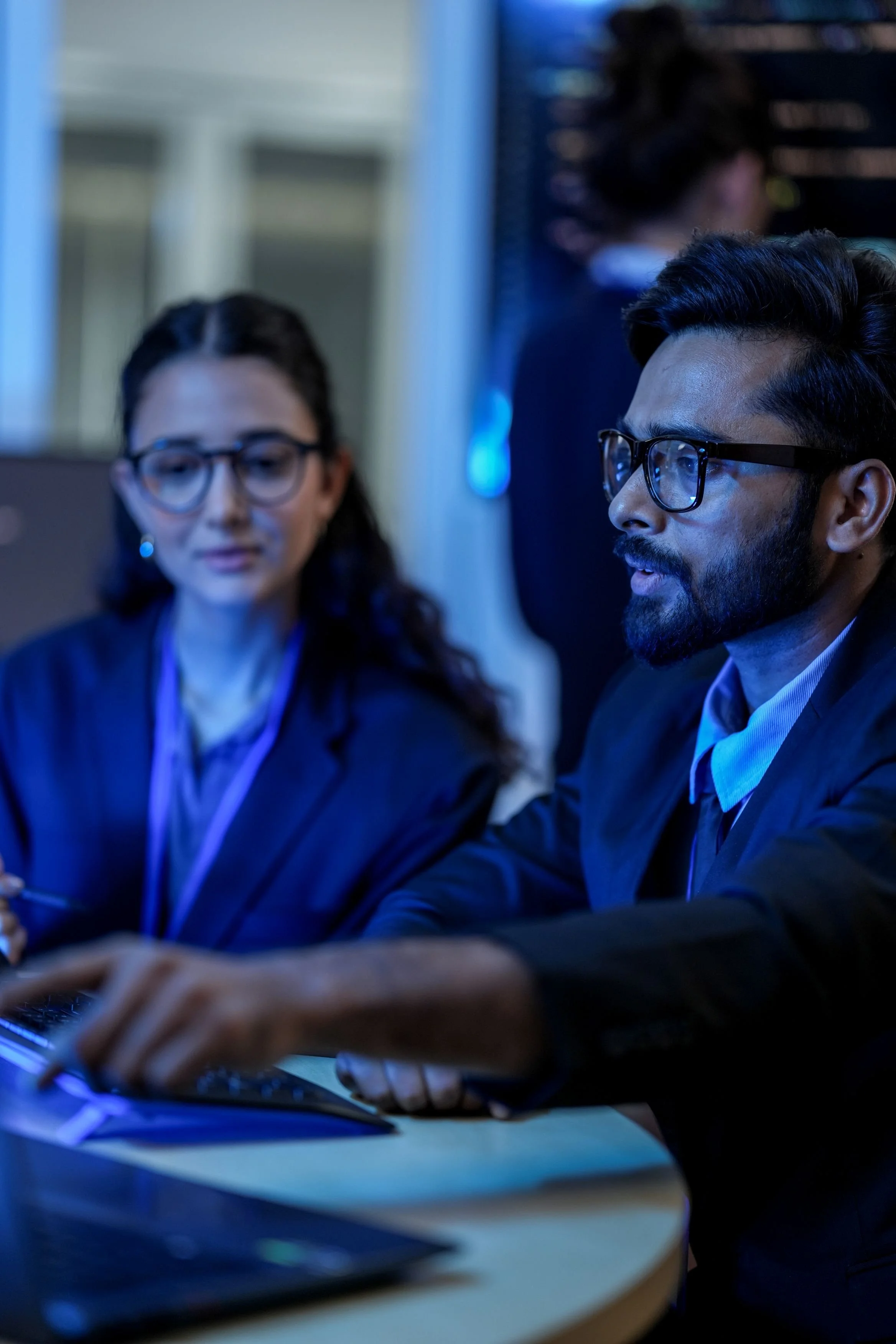 Two professionals in business attire working together at a desk with a computer in a modern office setting.