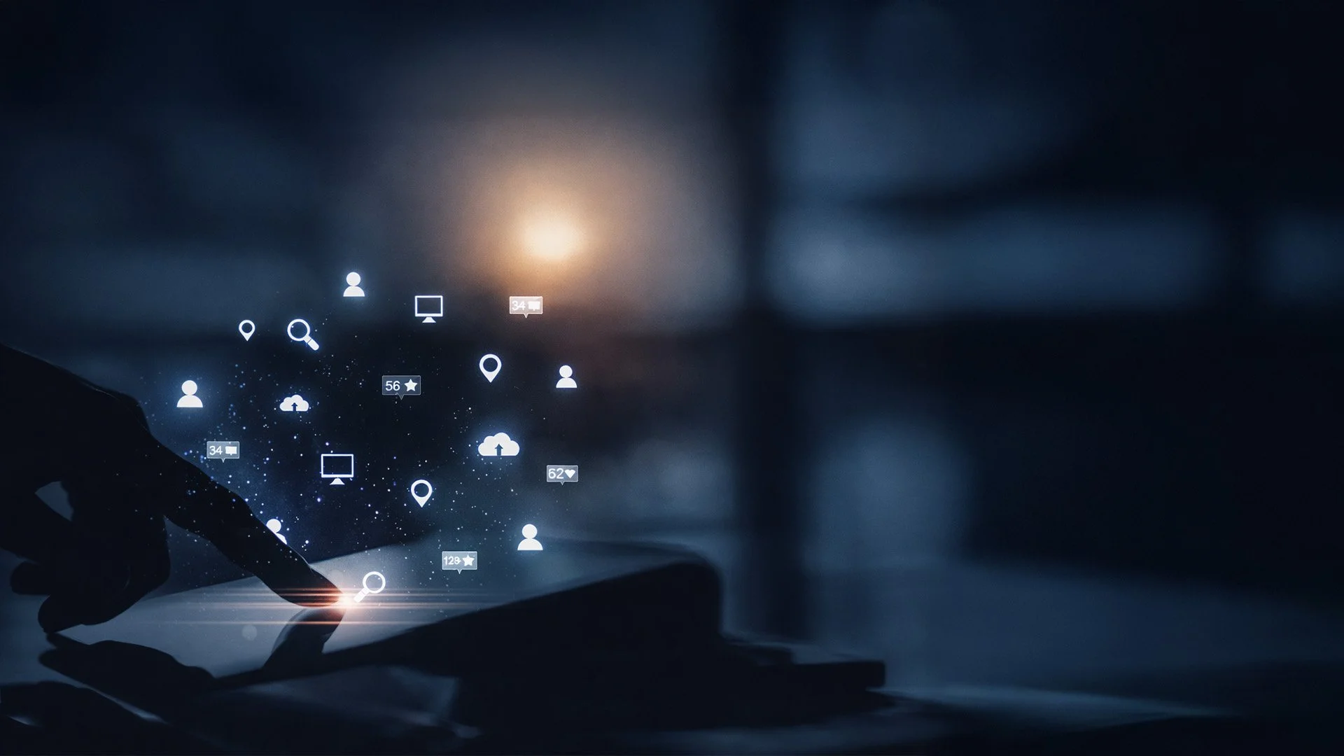 Silhouette of a hand touching a tablet screen with floating digital icons representing cloud storage, communication, location, search, and social media in a dark setting.