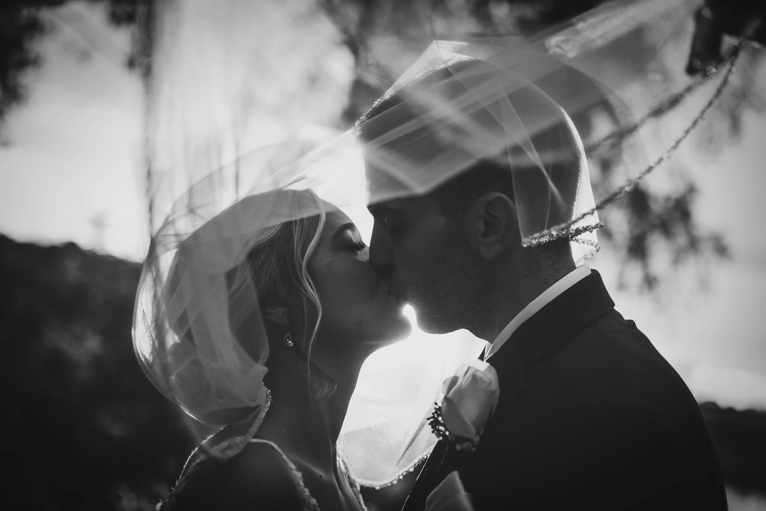 A black and white photograph of a couple kissing, with the woman wearing a wedding veil and the man dressed in a suit.