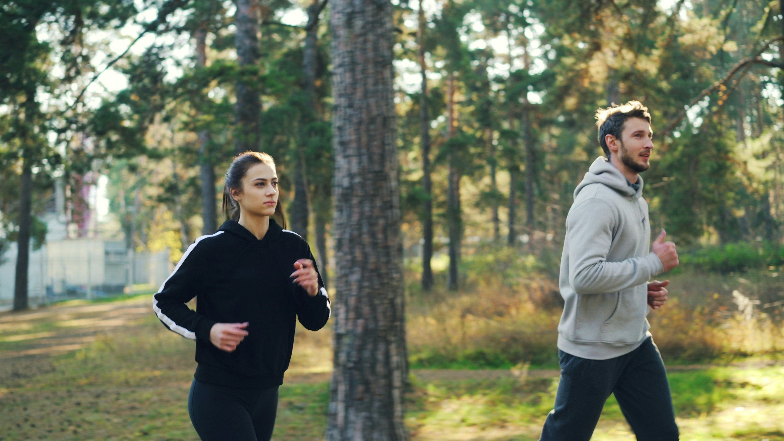 A man and woman jogging in a wooded park during daytime.