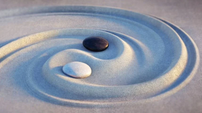 Two stones, one black and one white, placed on a sand surface creating a ripple pattern.