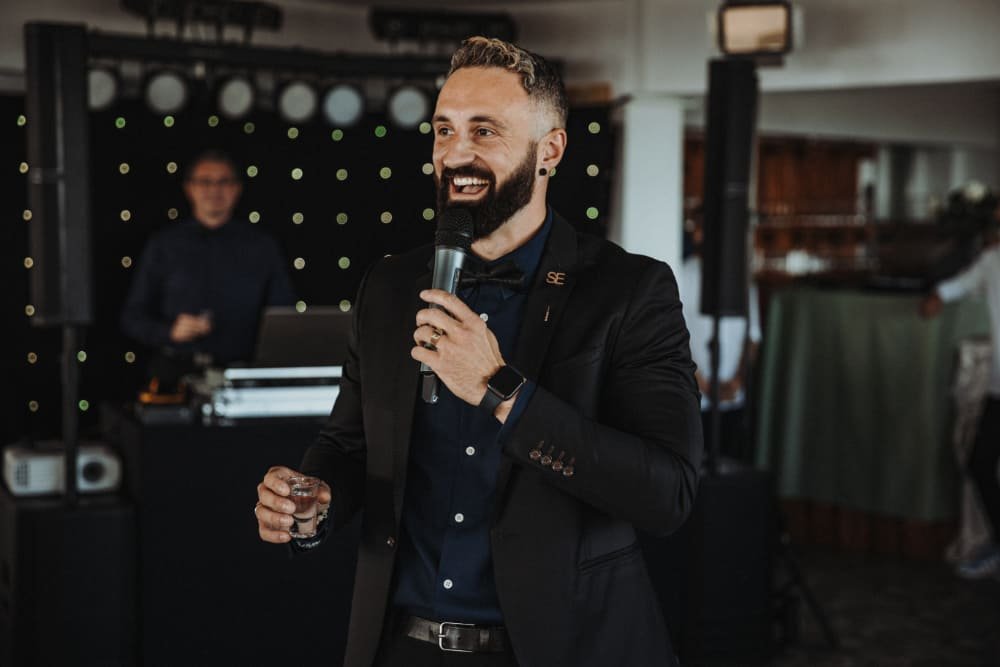 Ein lachender Mann iim Anzug Tamada Stas als Hochzeitsmoderator und Wedding Host auf einer deutsch russischen Hochzeit mit DJ beim moderieren