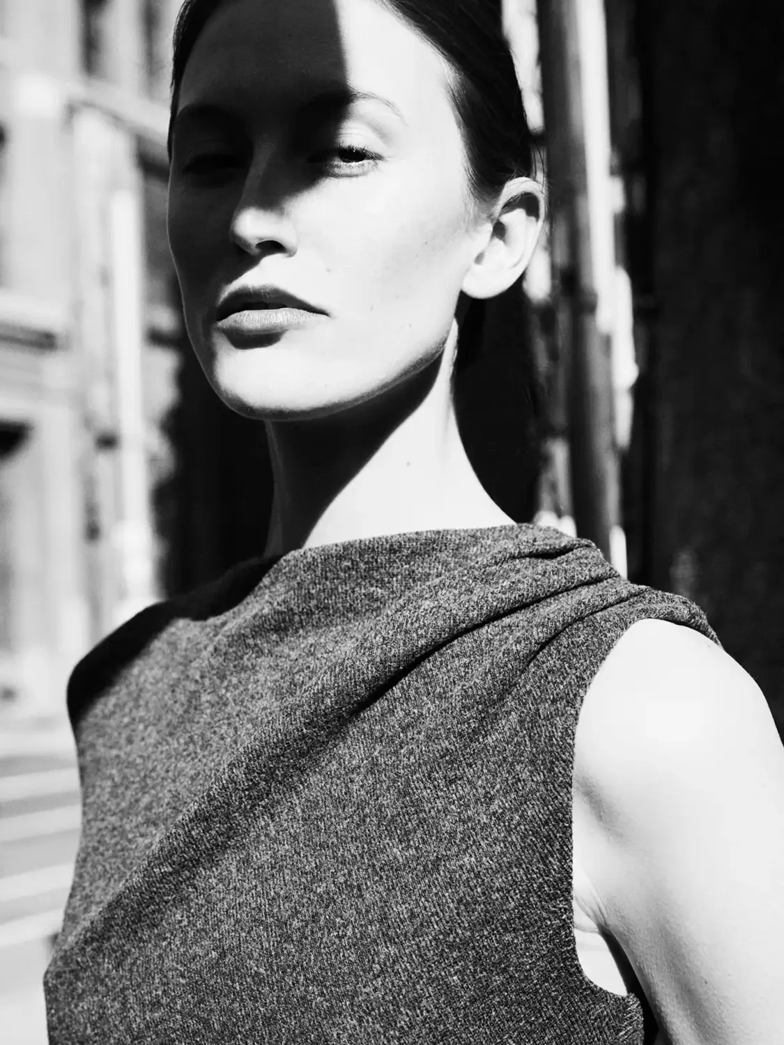 Black and white beauty shot  of a woman taking a selfie outdoors, with sunlight partially shadowing her face.