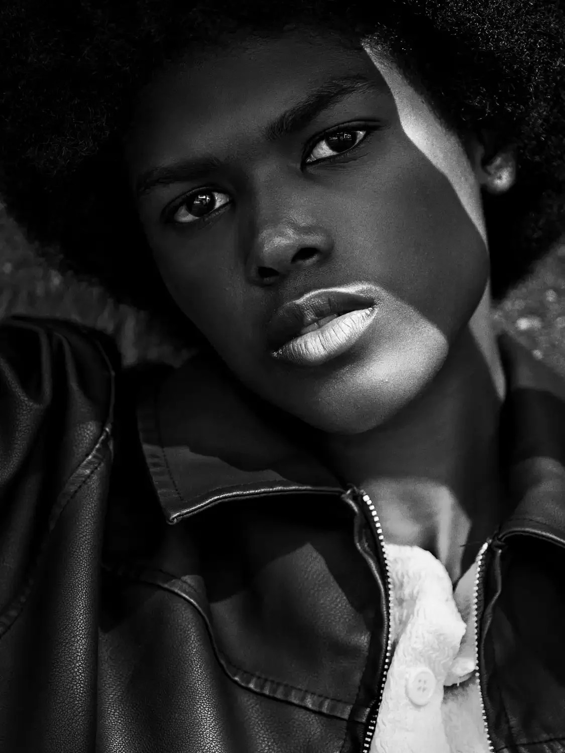 Black and white beauty shot of a black model woman wearing a white shirt and an leather jacket looking intently at the camera in. beautiful lighting.
