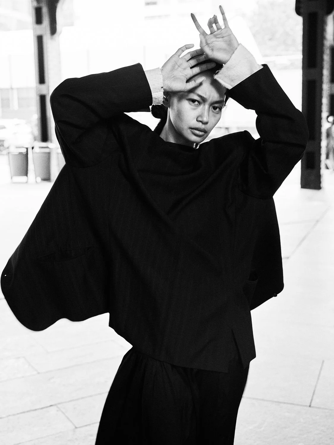 A woman in black clothing making a hand gesture with her fingers on her head, looking directly at the camera.