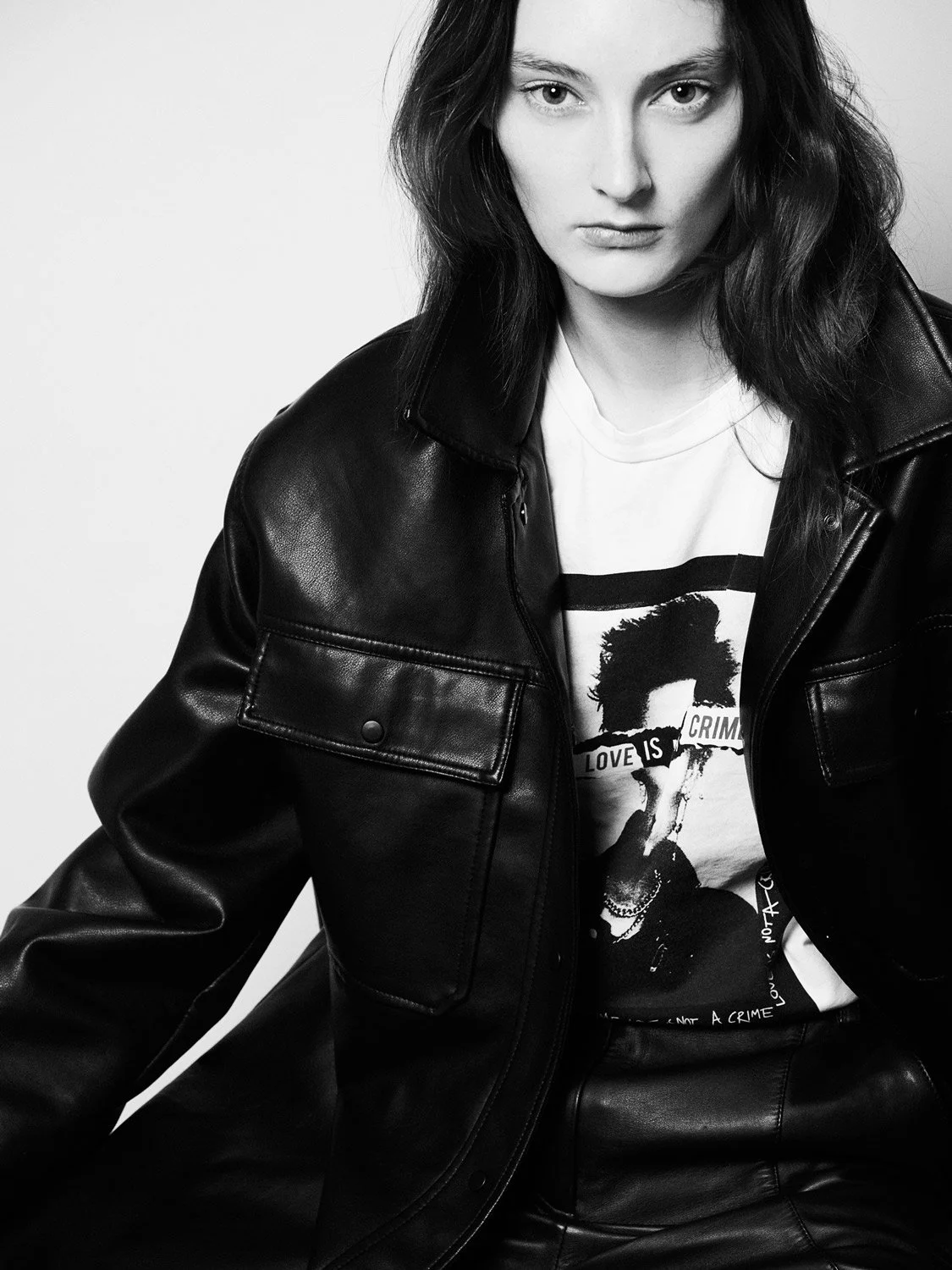 Black and white photo of a young woman with dark hair, wearing a leather jacket and a graphic T-shirt, looking directly at the camera.