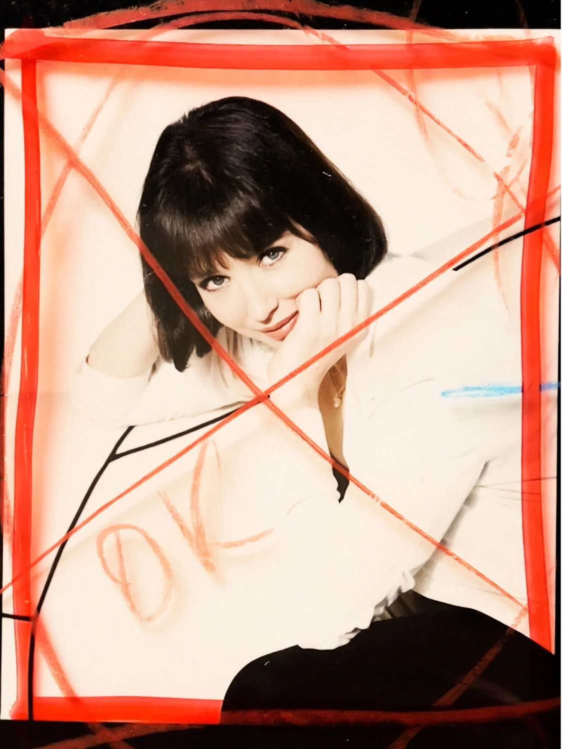 Photograph of a woman with dark hair, smiling, with her chin resting on her hand, enclosed by red and black marker lines and scribbles.