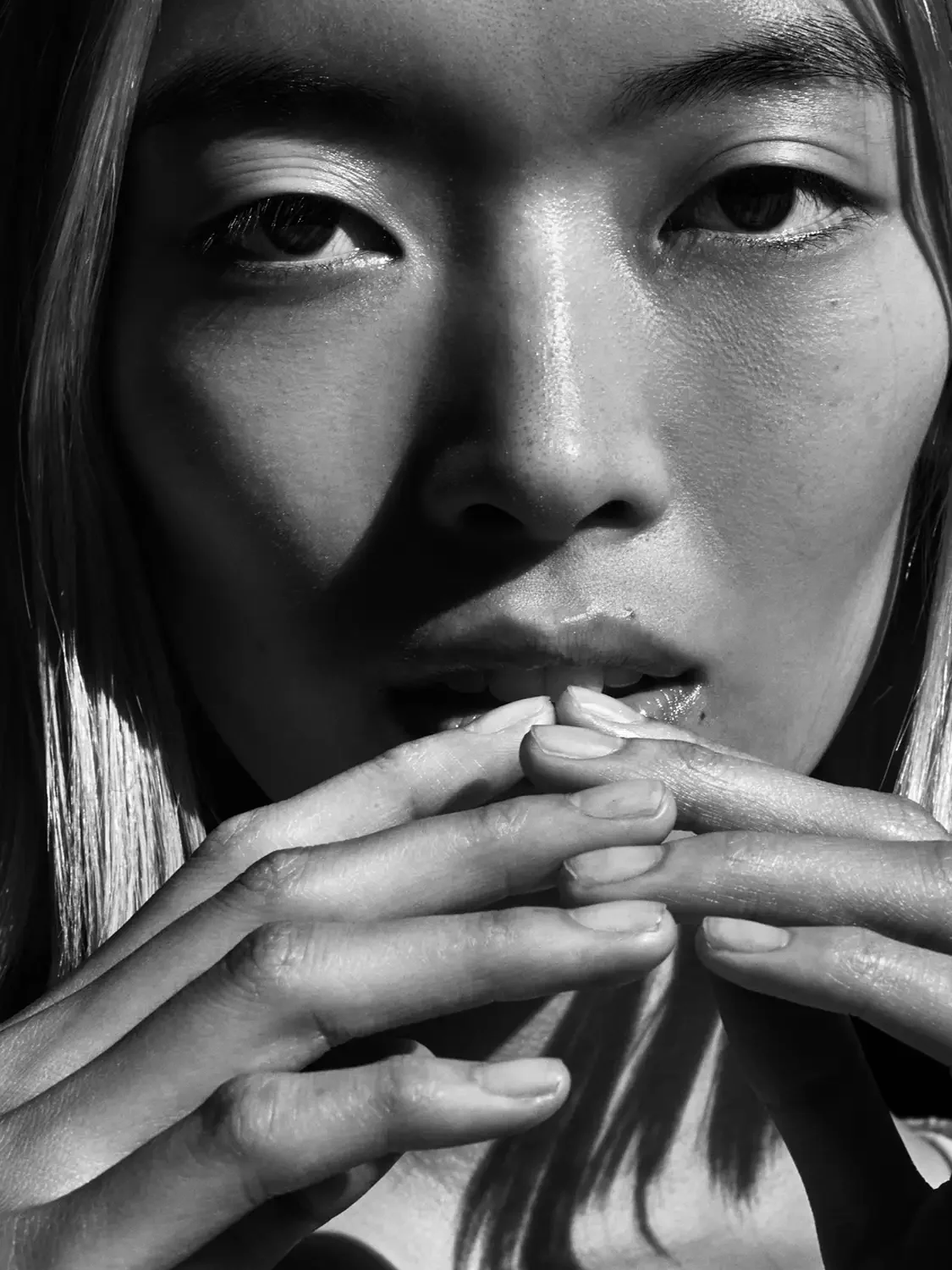 Asian woman with her hand up by her lips photographed in black and White.