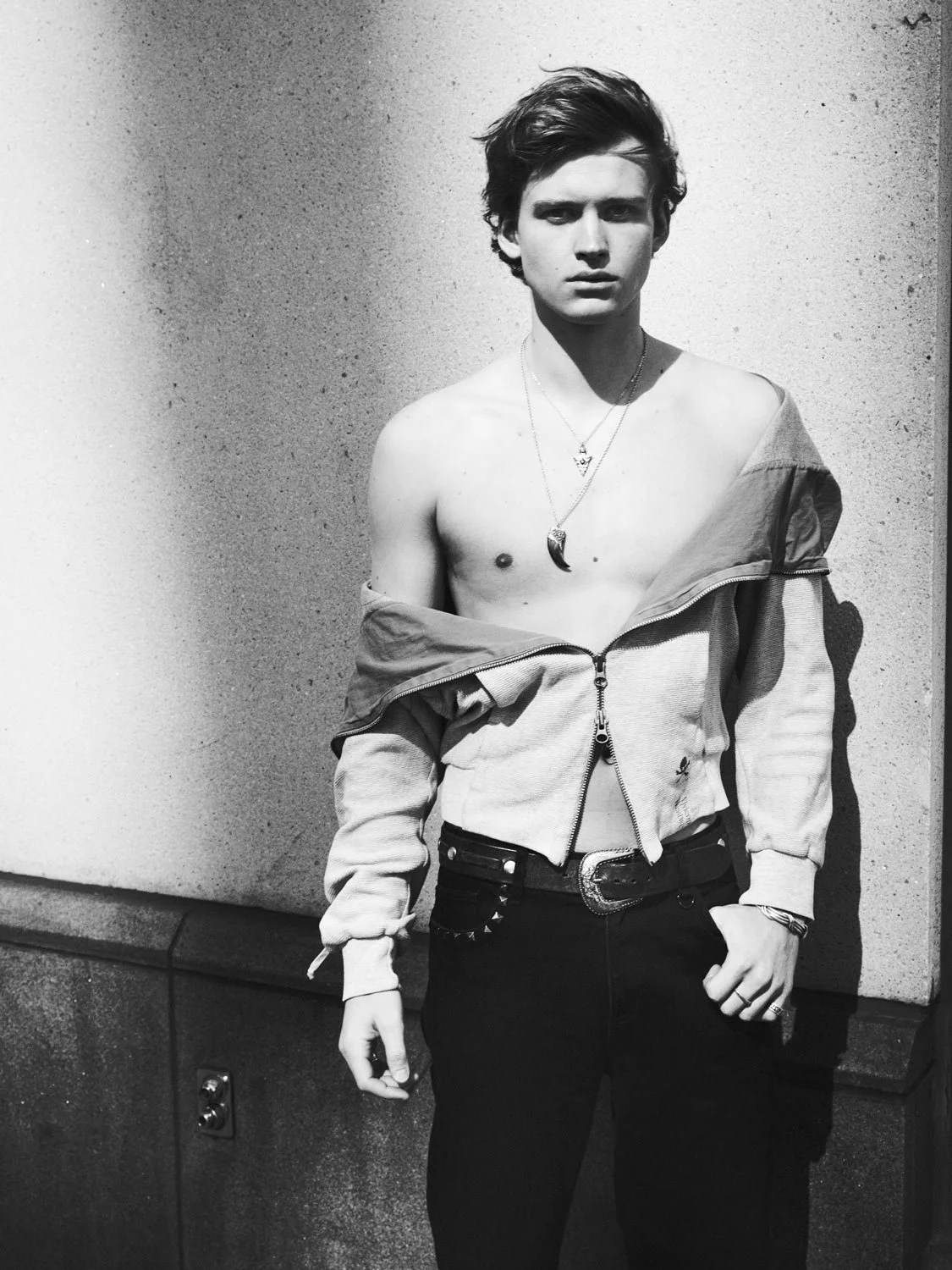 Fashion shot of a male model wearing a shirt off his shoulders  against a black and white wall.