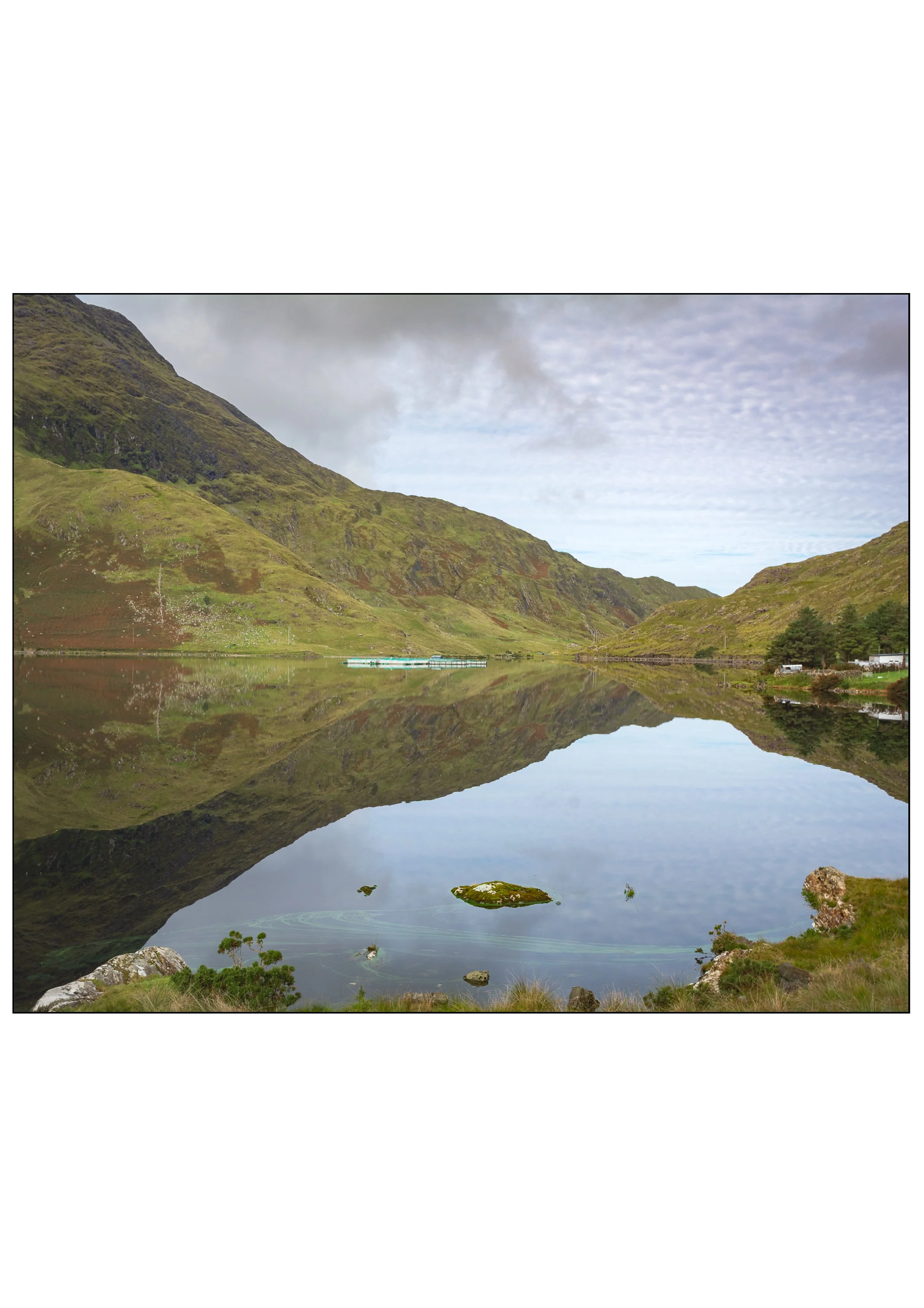 A serene lake in a valley, surrounded by green mountains, with the lake reflecting the mountains, sky, and clouds.
