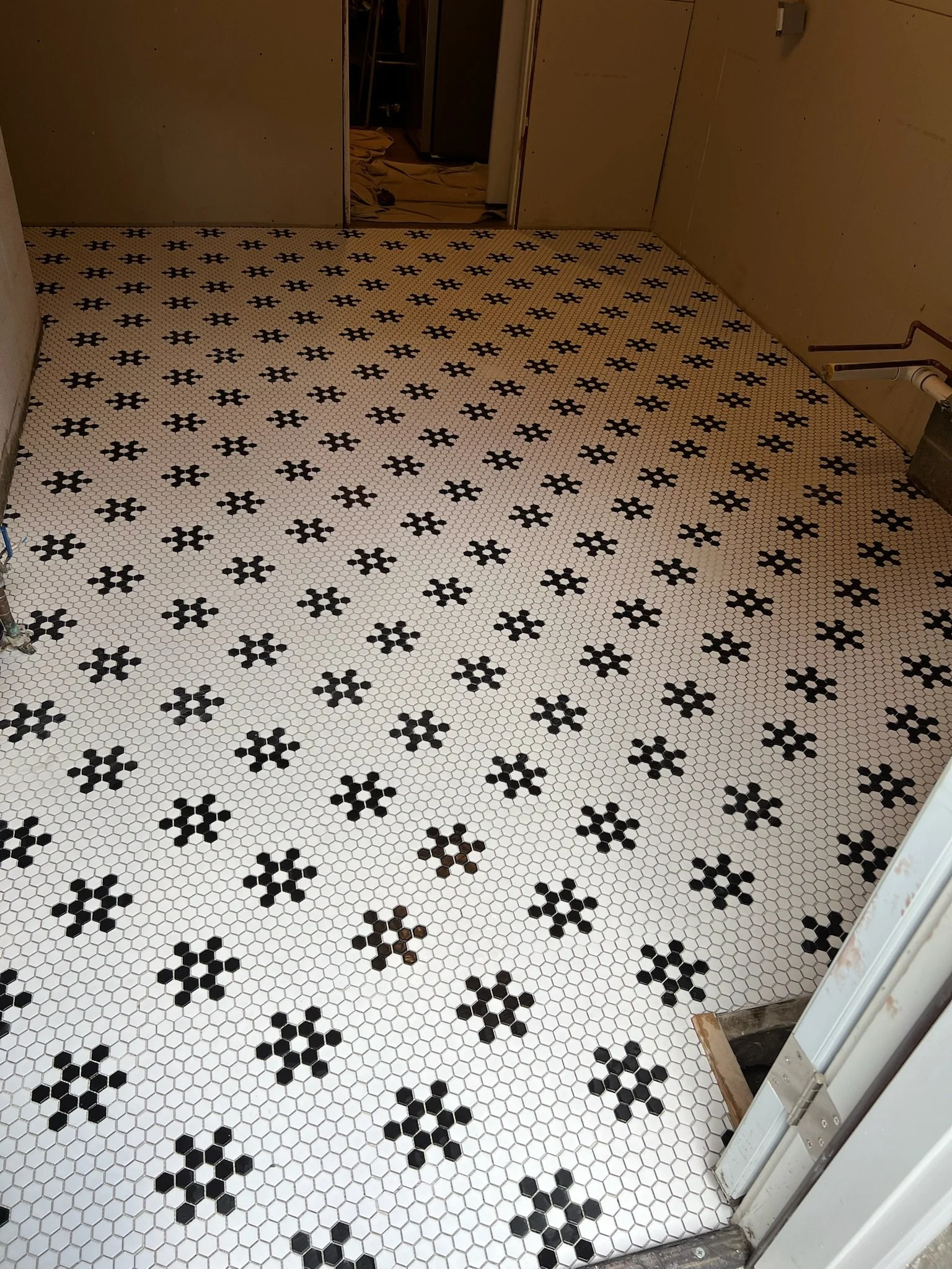 New white tile floor with black floral pattern at a construction site, with unfinished walls and doorways.