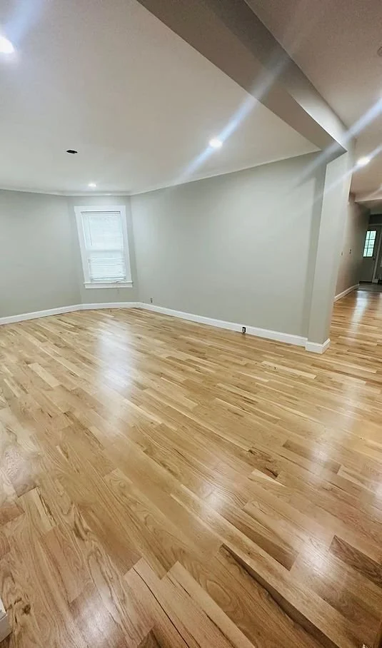 Empty living room with hardwood floors, white walls, a window, and ceiling lights.