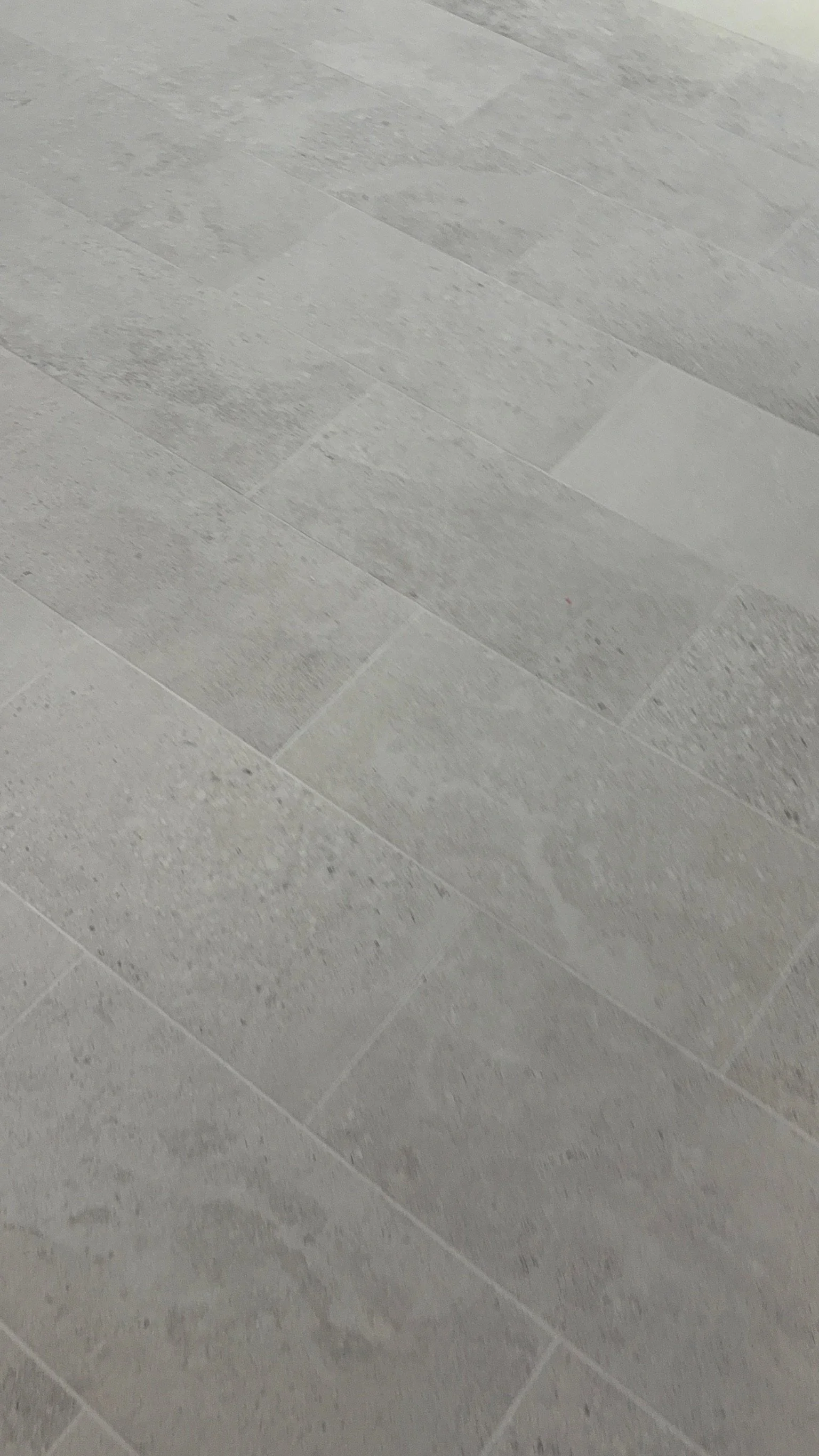 Close-up of a light gray tiled floor with rectangular tiles arranged in a staggered pattern.