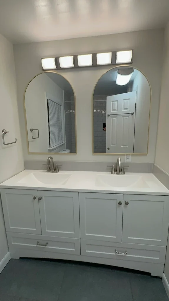 Bathroom with a double sink vanity, two mirrors, and modern light fixture.