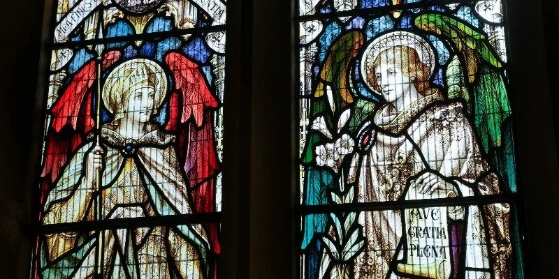 Stained glass window depicting two angelic figures with halos and robes, surrounded by decorative floral and geometric patterns.