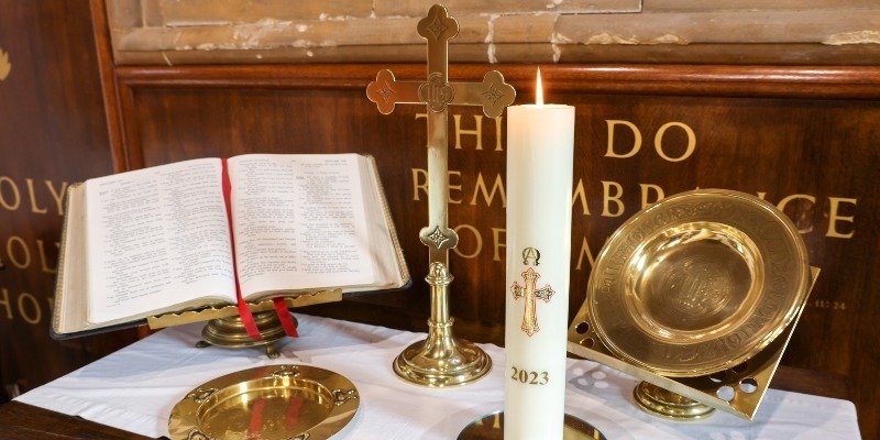 Church altar with open Bible, cross, lit candle, and gold-plated bowl and plate.